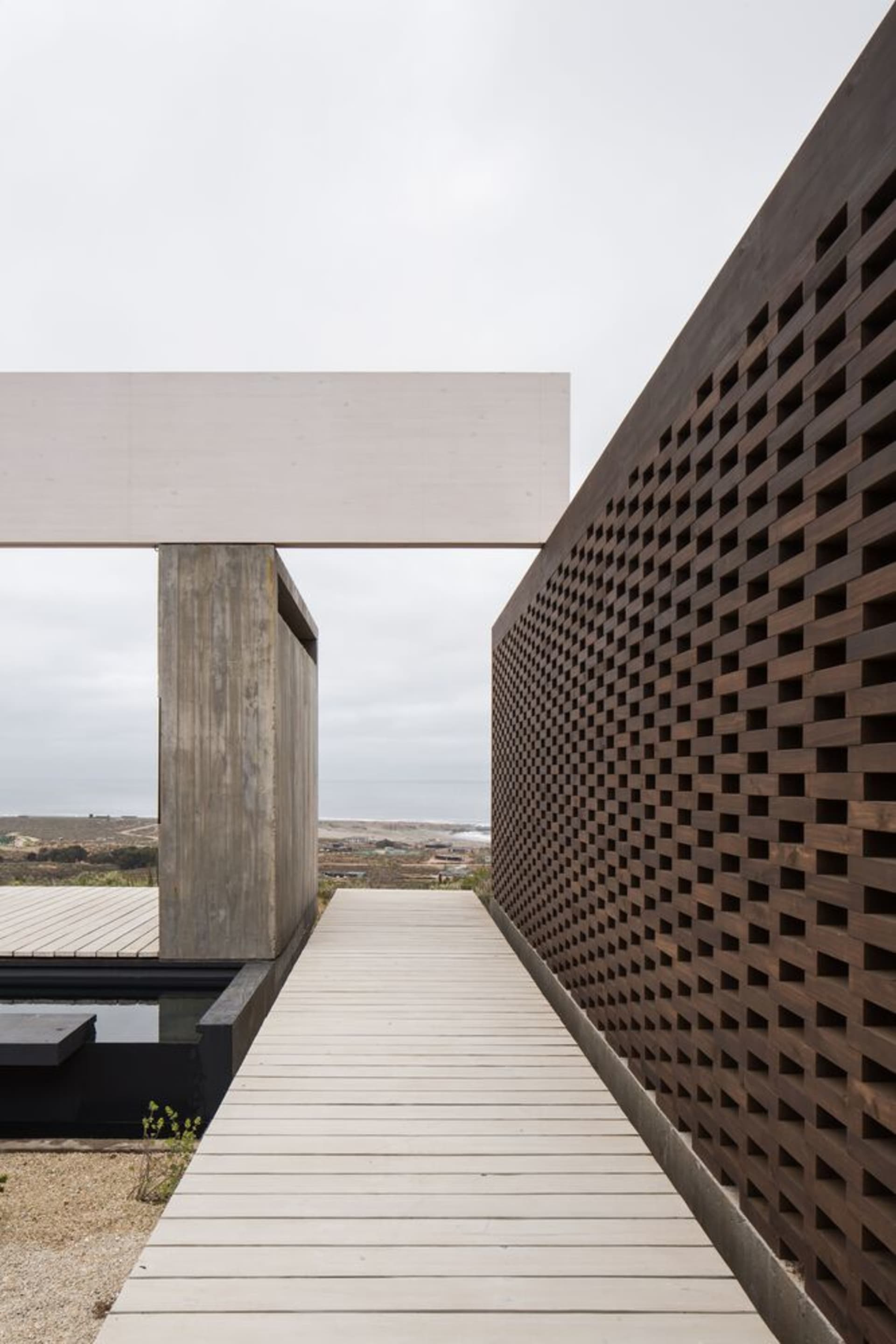 A modern building exterior featuring a concrete structure with a wooden walkway and a perforated wooden wall.