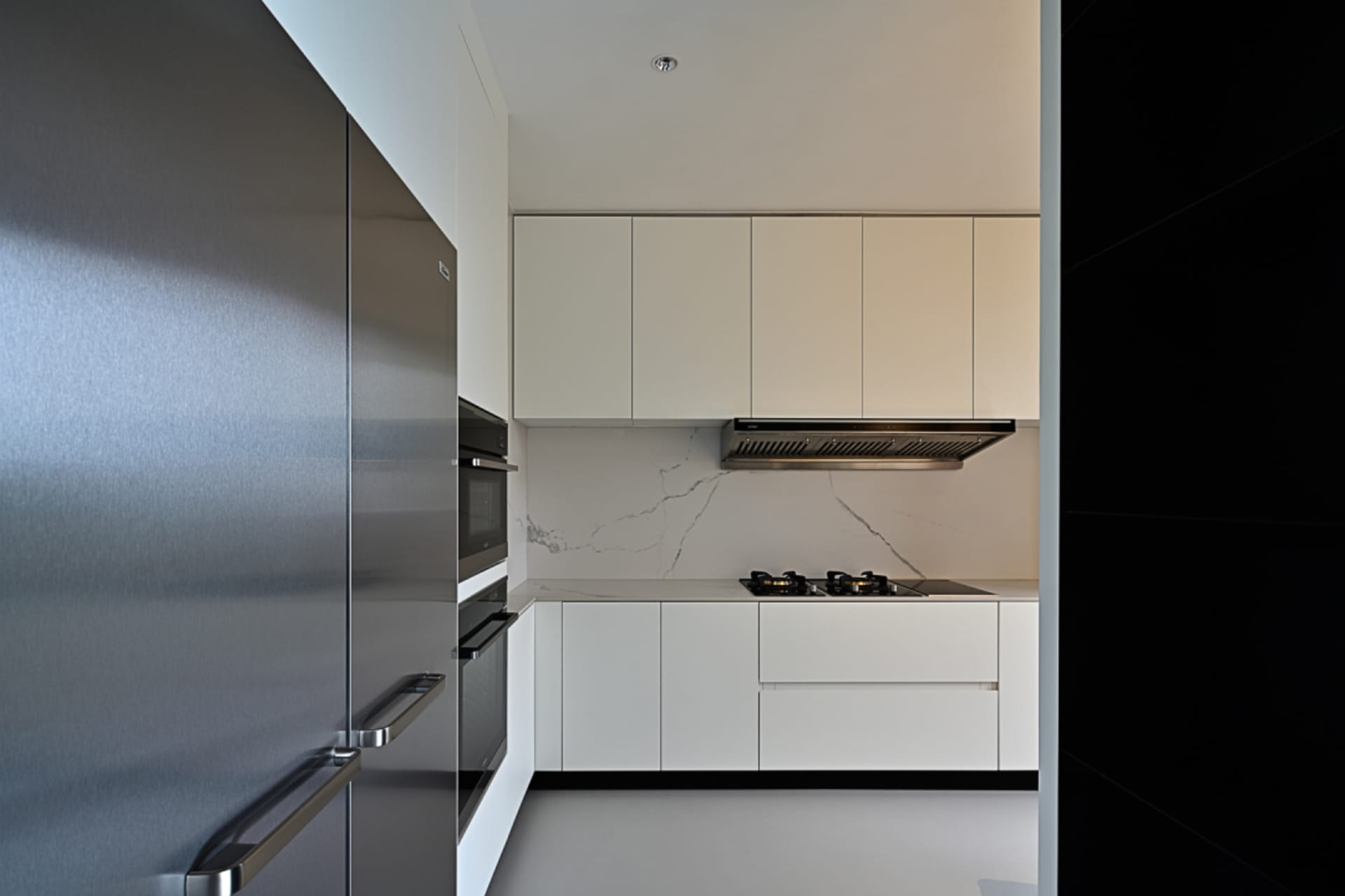 A modern minimalist kitchen with white cabinets, stainless steel appliances, and a marble backsplash.