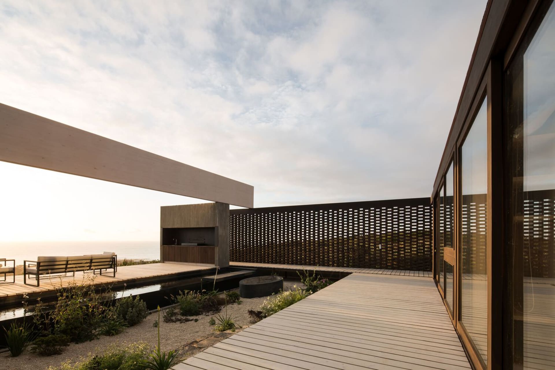 Modern residential exterior featuring a wooden deck, metal fencing, and glass walls.