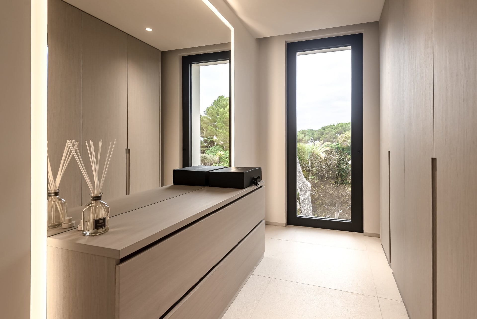 Modern minimalist closet space with wooden cabinets, glass windows, and a mirror.