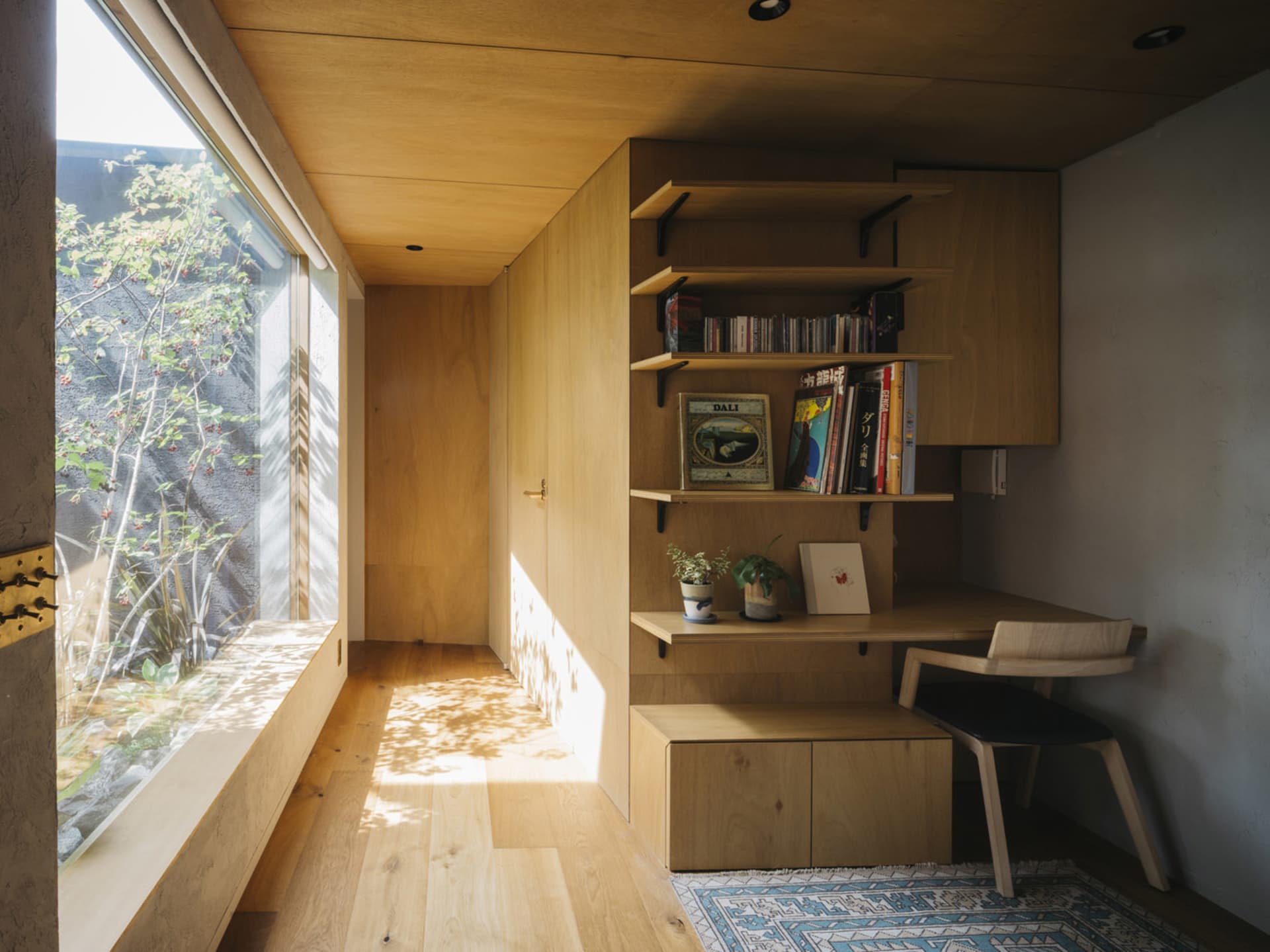A modern home office featuring wooden furniture and shelves, with a window and natural light.