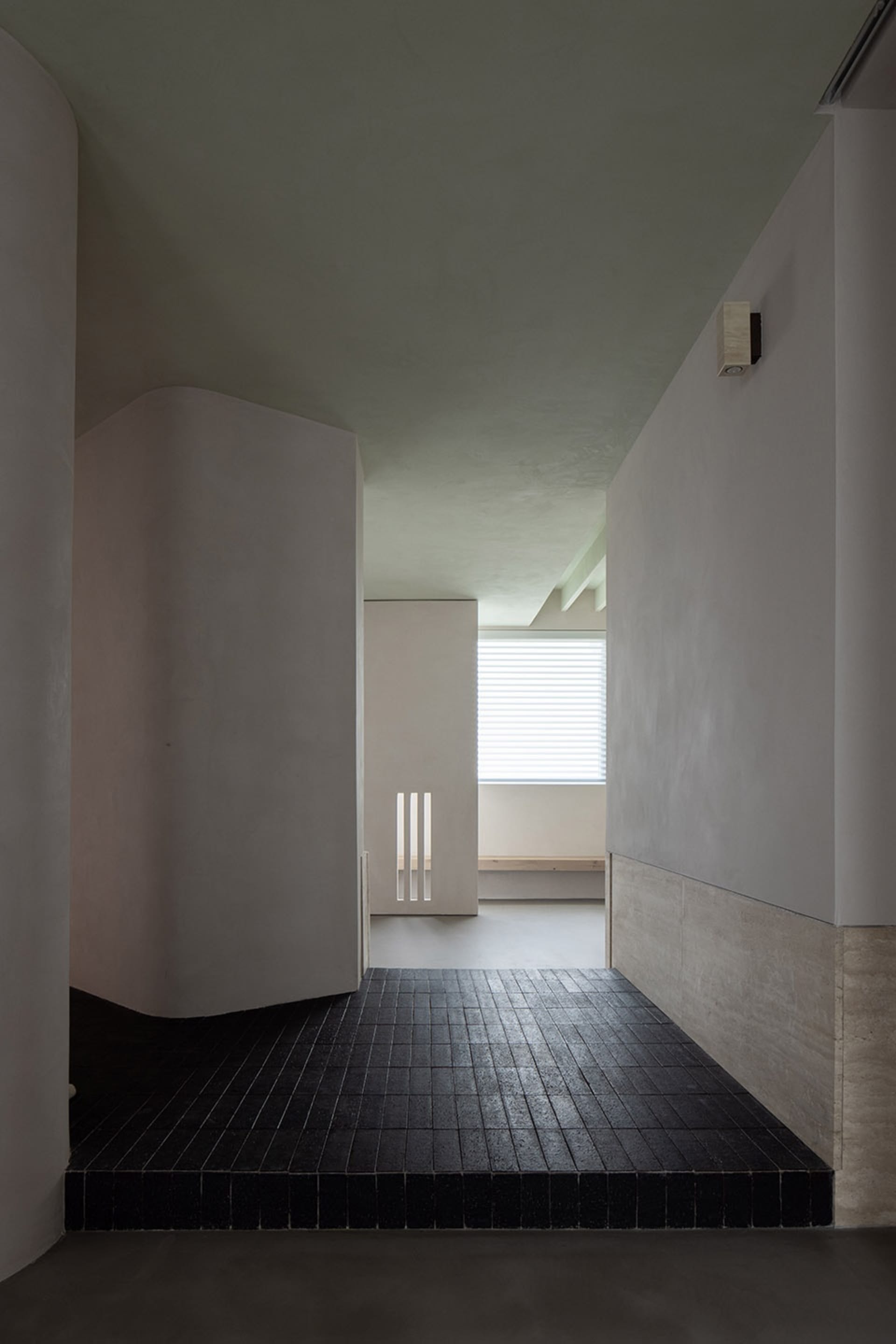 A modern, minimalistic corridor with a concrete floor, white walls, and a window with blinds.