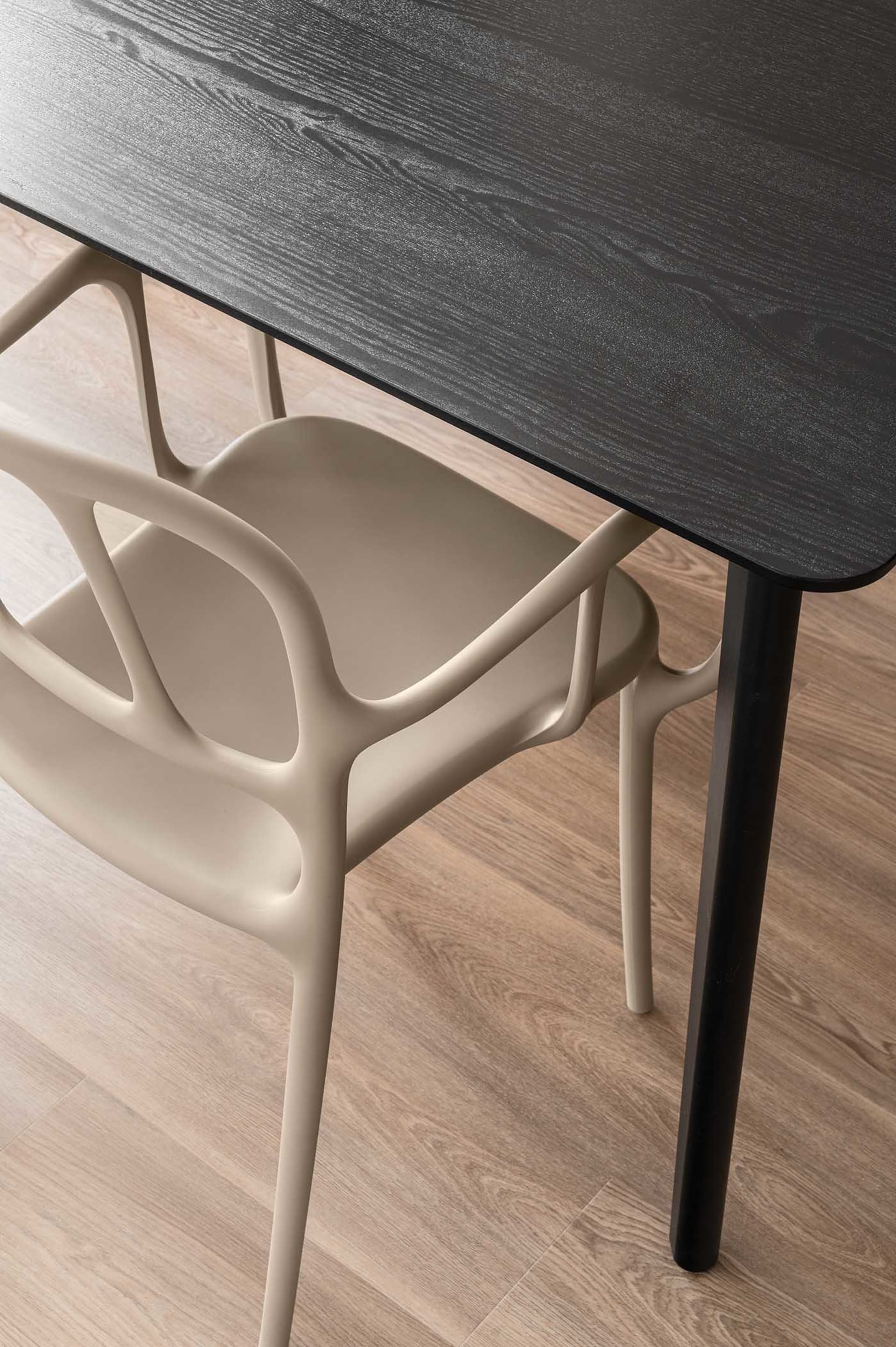 A modern dining room with a black wooden table and a beige, ergonomic chair.