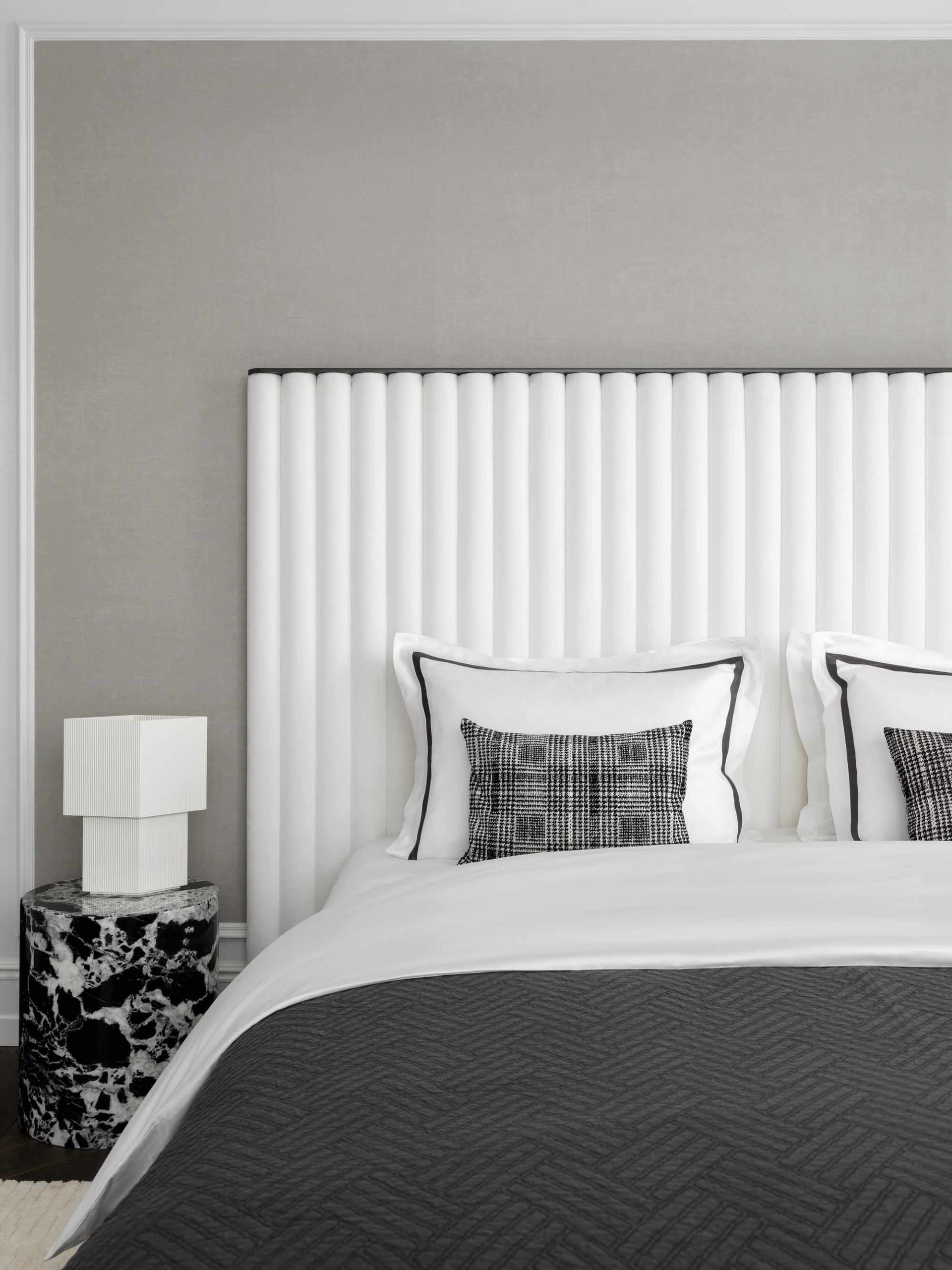 A minimalist bedroom featuring a white fabric headboard and a marble side table.