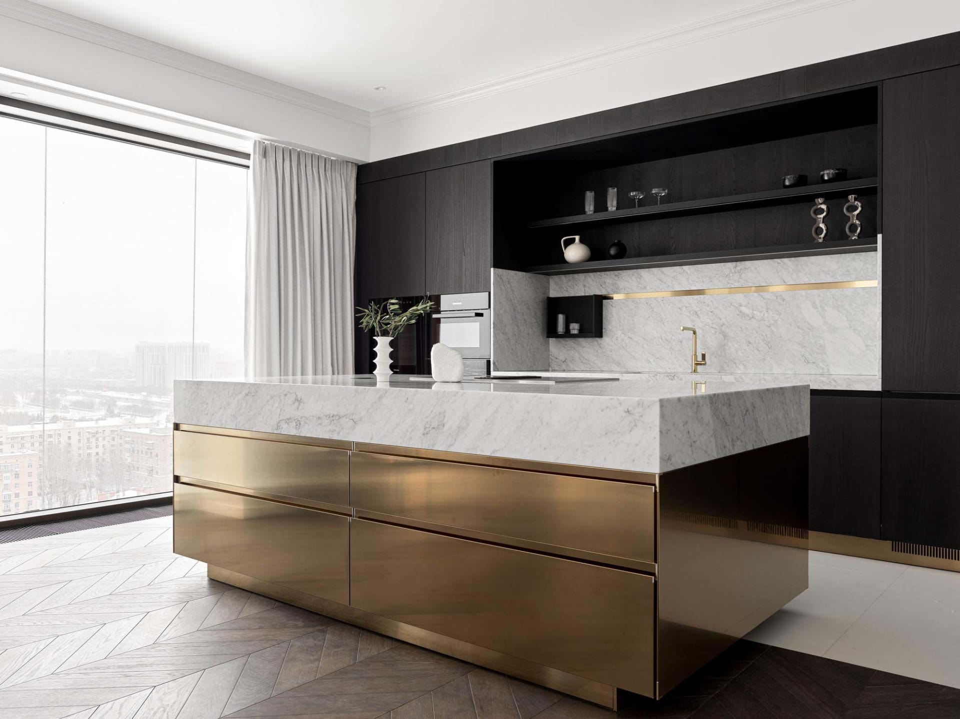 Modern kitchen with marble countertops, brass accents, and a large window.