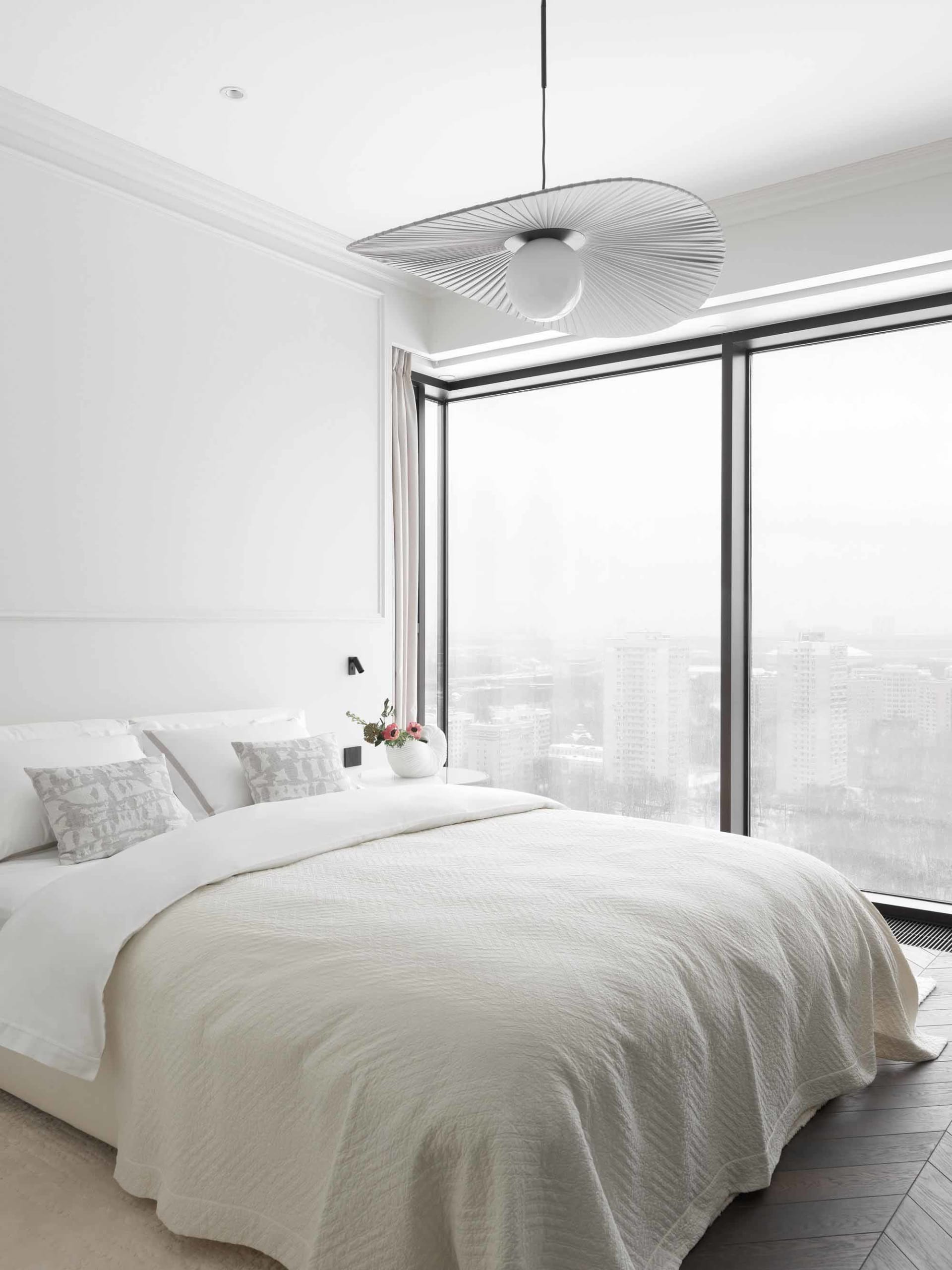 A minimalist bedroom featuring a white textured cotton blanket on a bed with a panoramic window showing a cityscape.