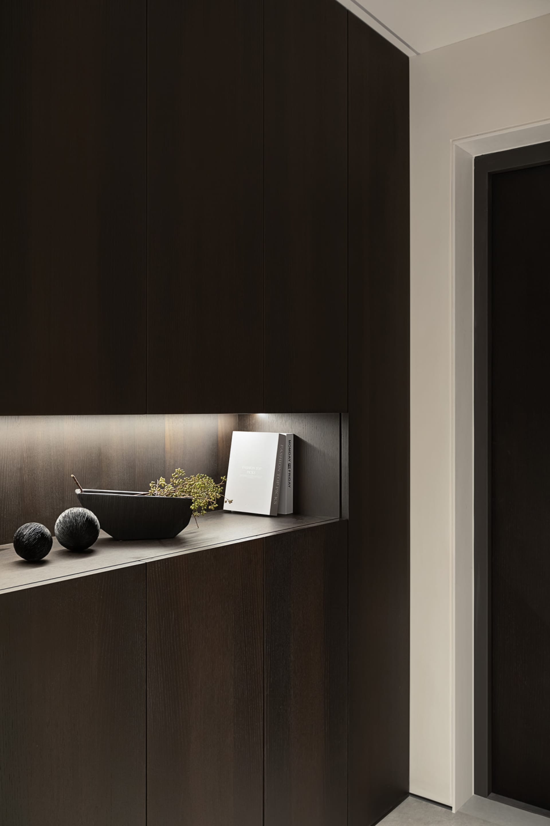 A modern cabinet made of dark wood with a shelf displaying decorative items, including a black bowl, a black spherical orname