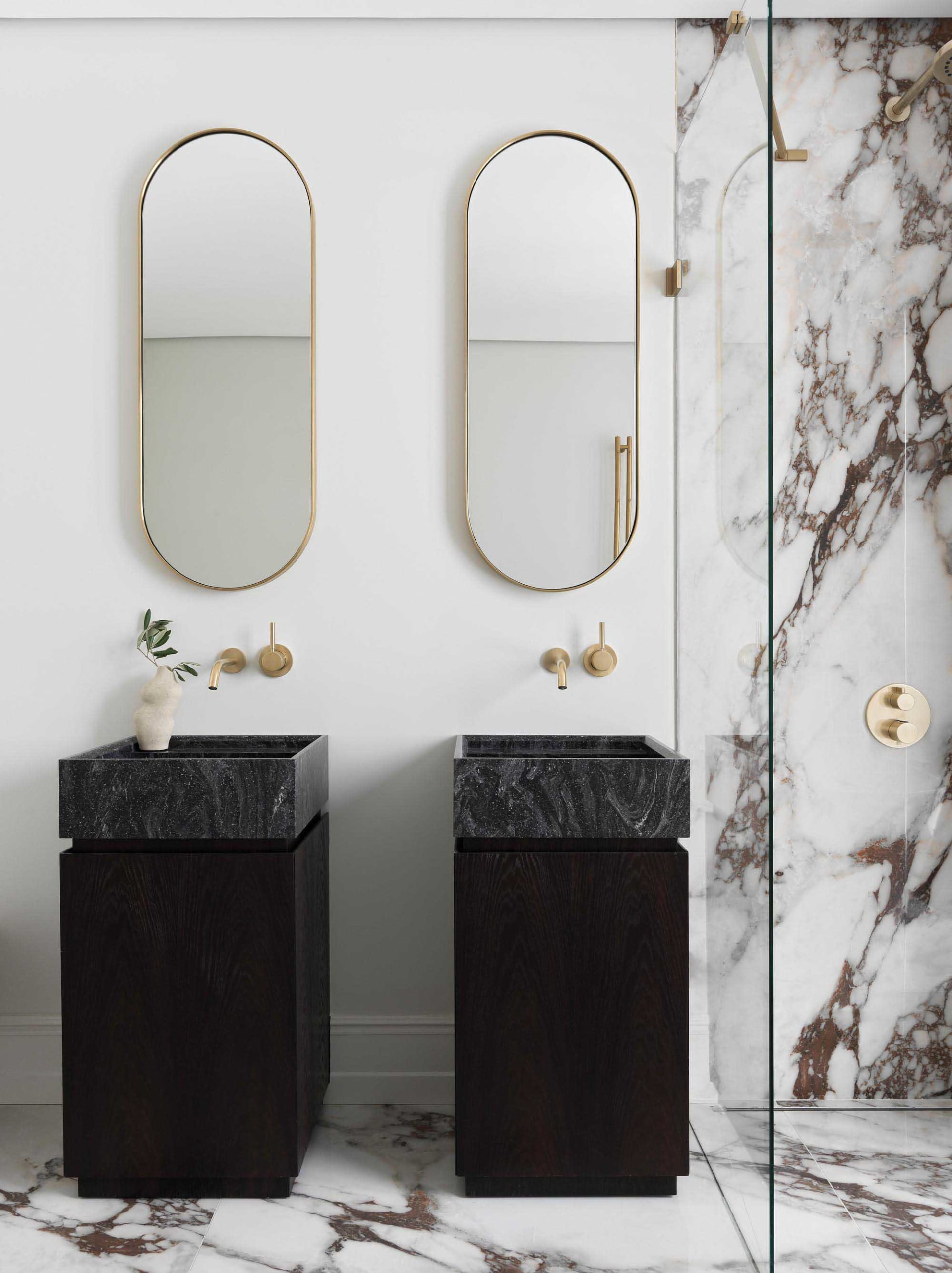 Modern minimalist bathroom with black marble sinks, brass fixtures, and marble walls and floor.