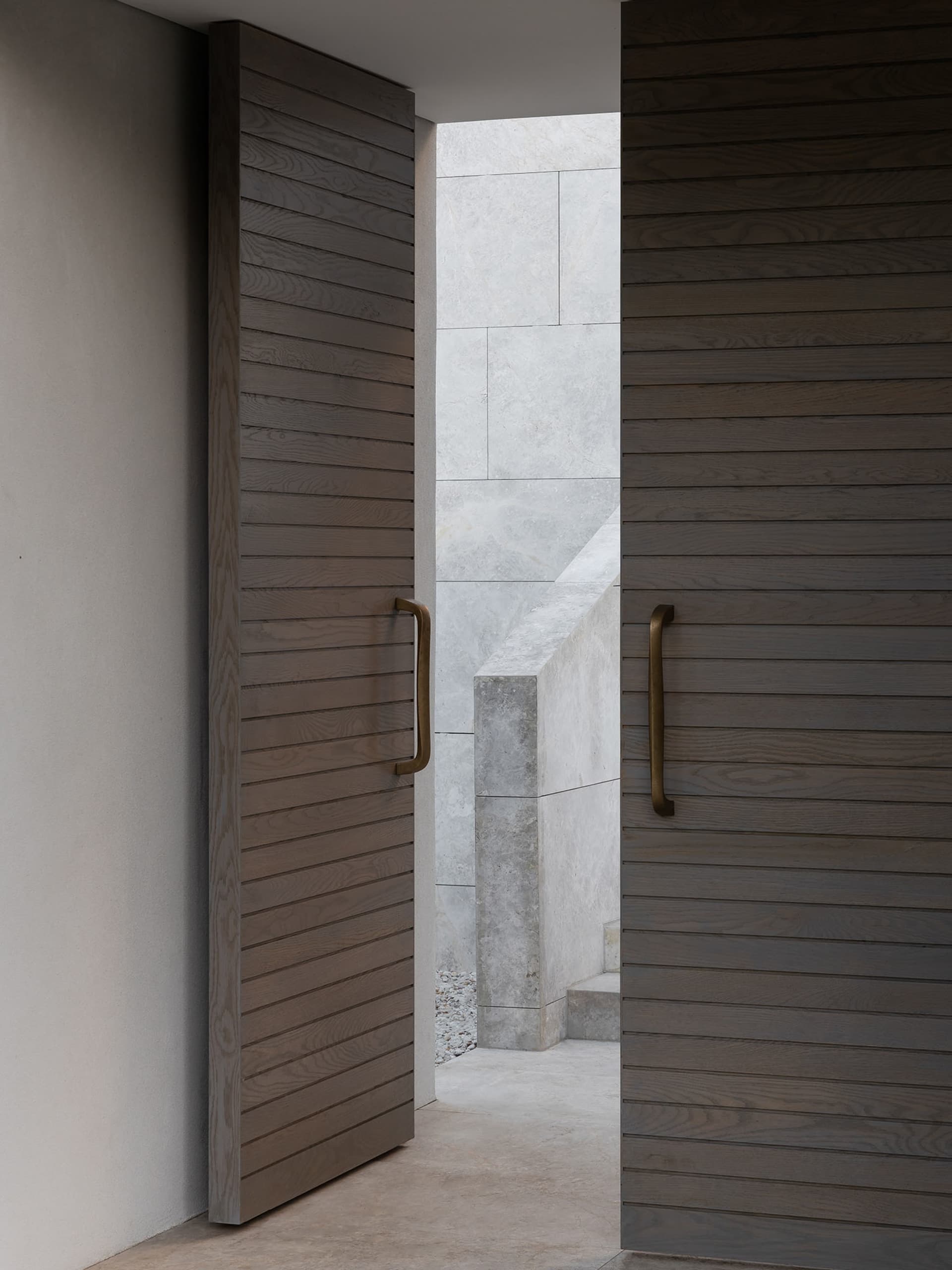 A modern doorway featuring wooden and metallic materials, leading into a light-filled space with a white wall and stone steps