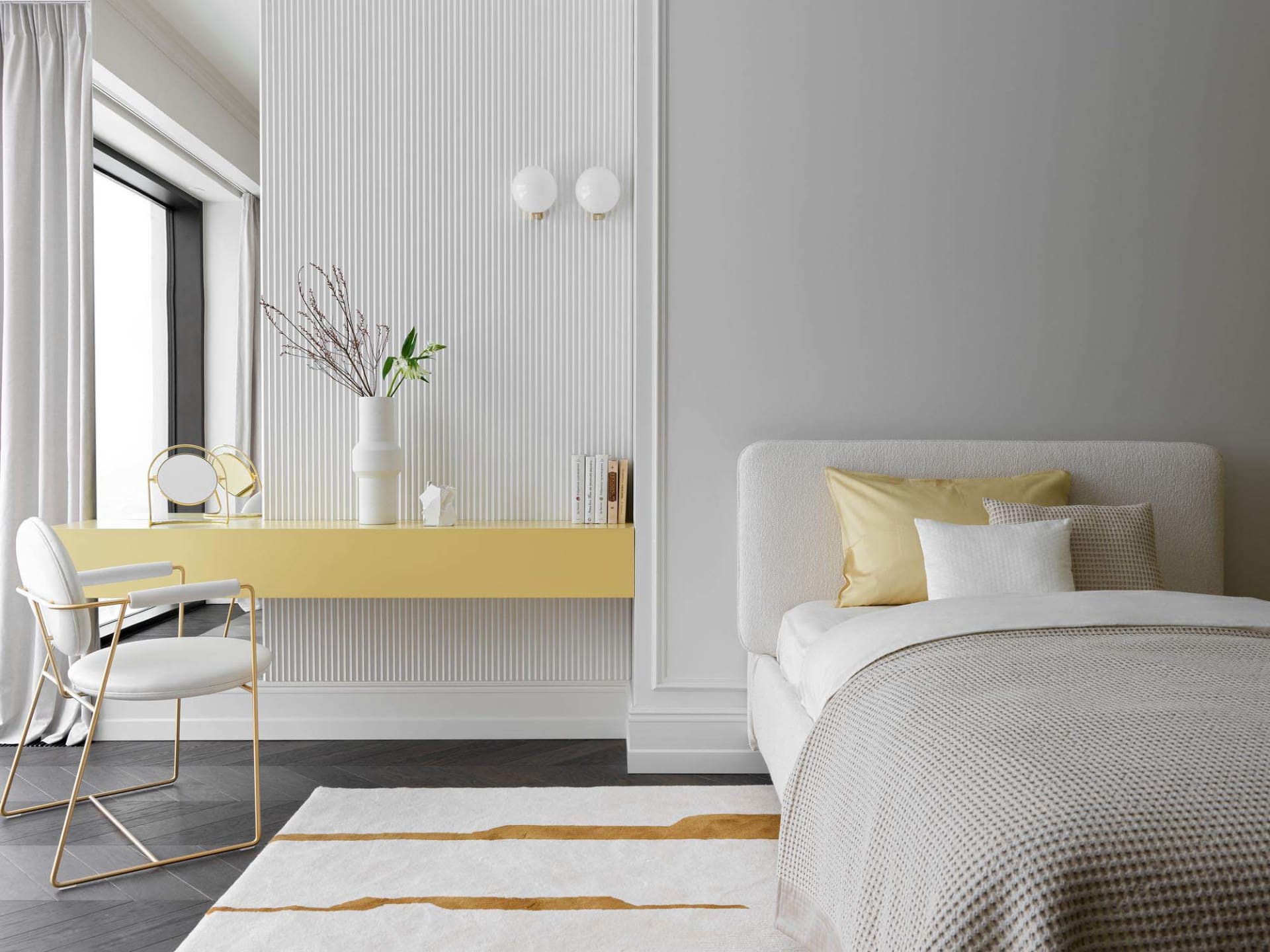 A modern bedroom featuring a textured wallpaper wall, a white bed with yellow pillows, a yellow desk with a vase and books, a