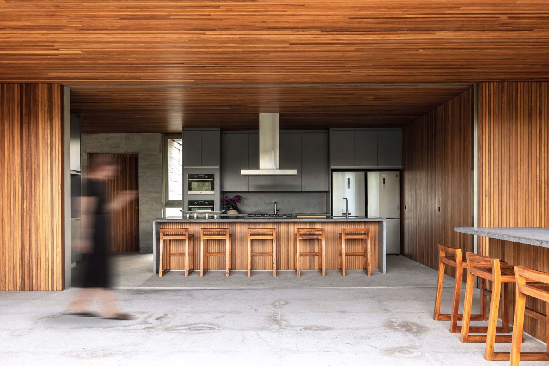 Modern kitchen with wooden cabinets, countertops, and stools.