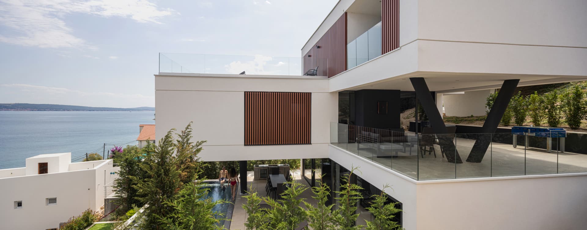 A modern residential exterior featuring glass walls and a swimming pool overlooking the sea.
