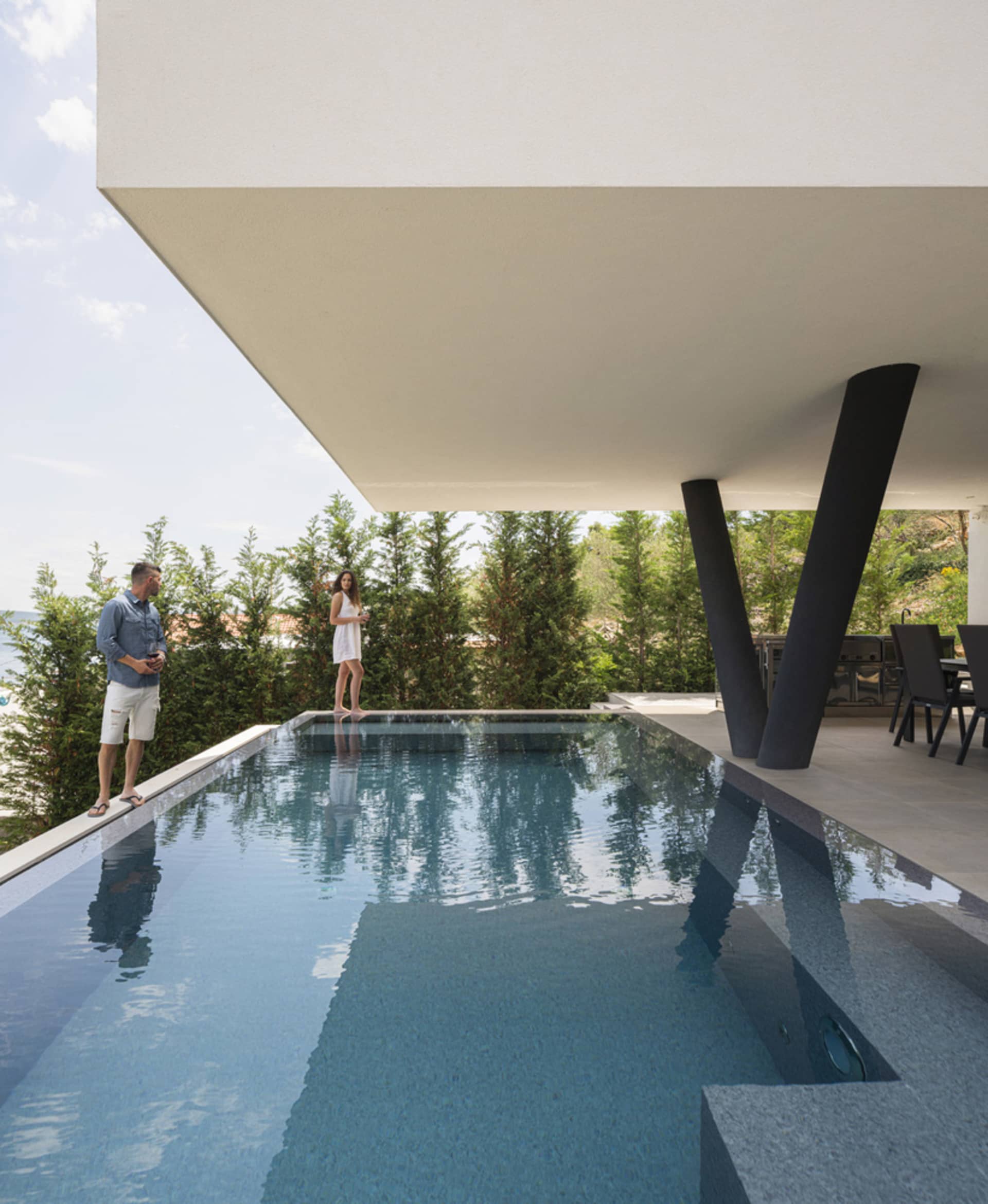 A modern swimming pool with concrete walls and a covered patio area.
