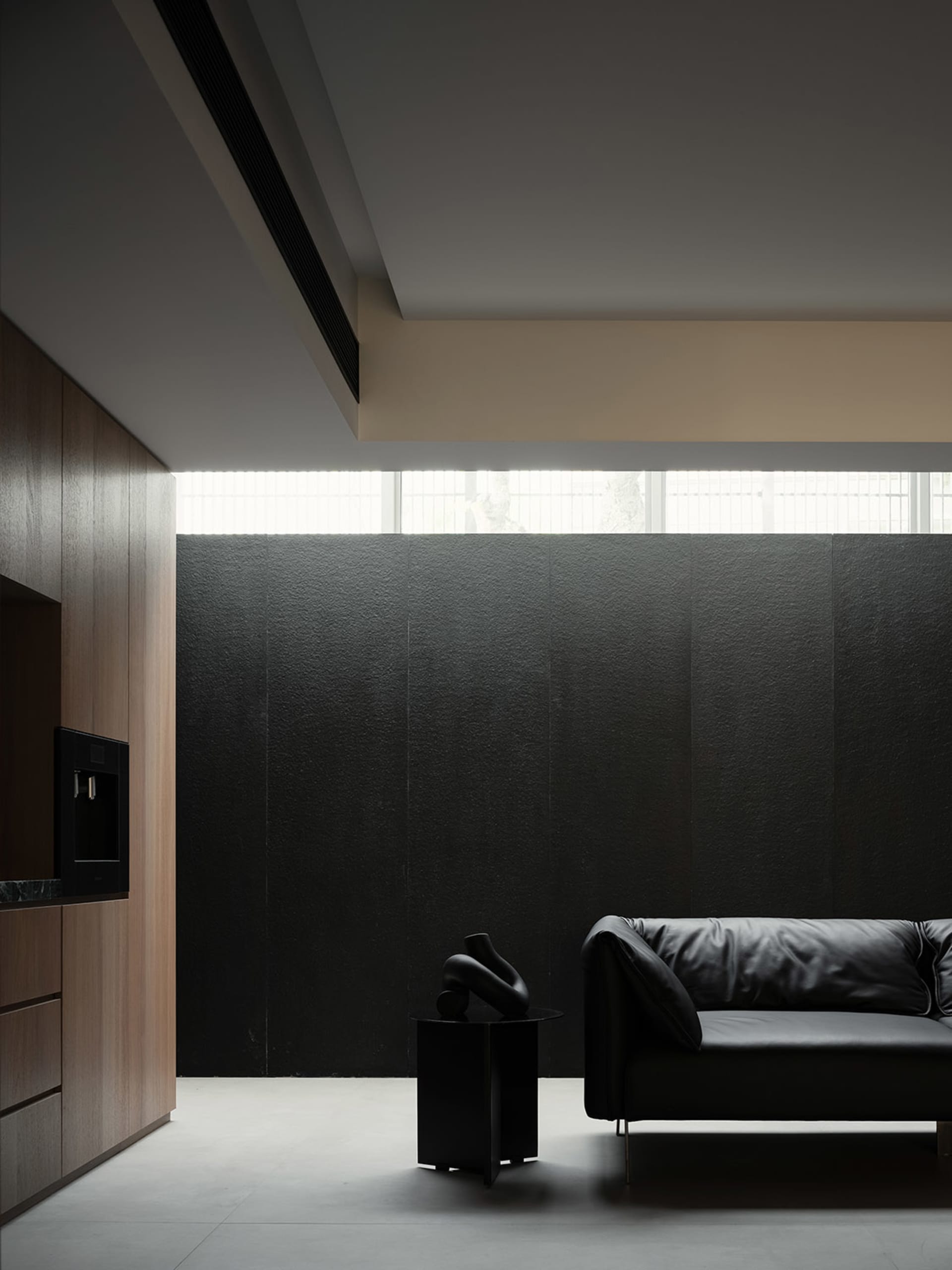A modern interior design featuring a black leather sofa against a textured black wall, complemented by sleek wooden cabinets 