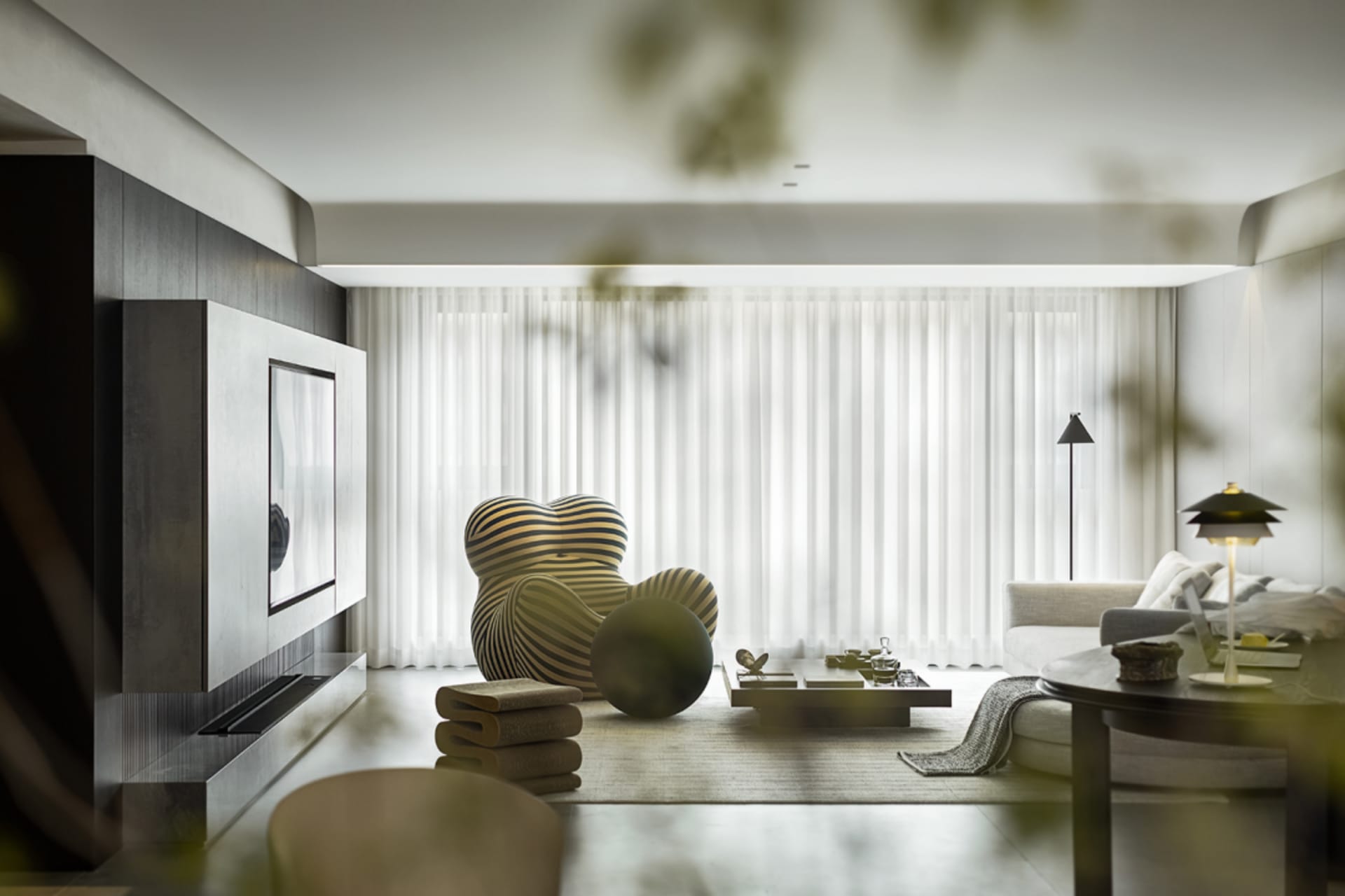 Modern minimalist living room with neutral tones, featuring a cozy armchair, low coffee table, and a sleek entertainment unit