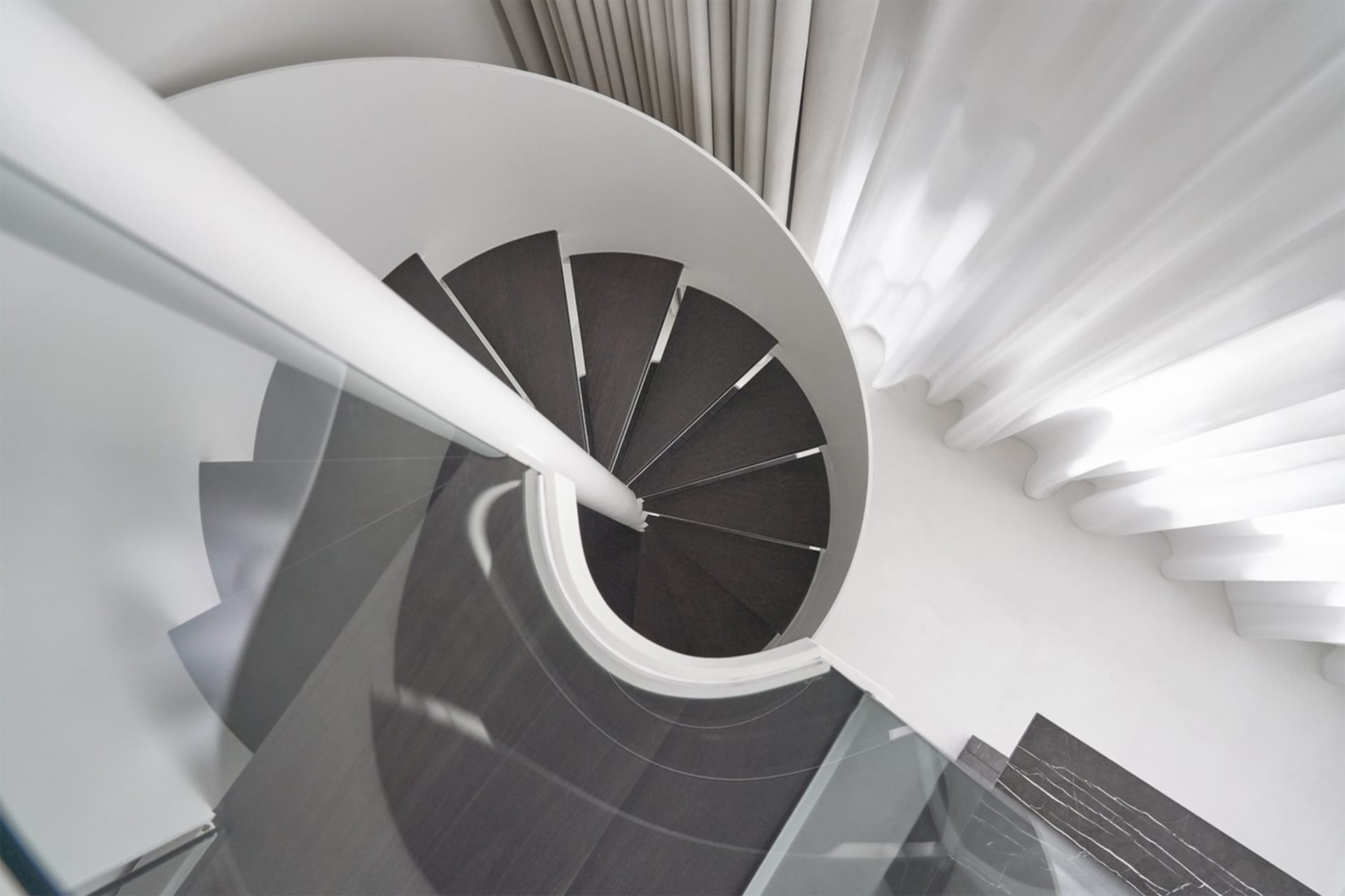 A modern wooden staircase in a white interior space with white curtains.