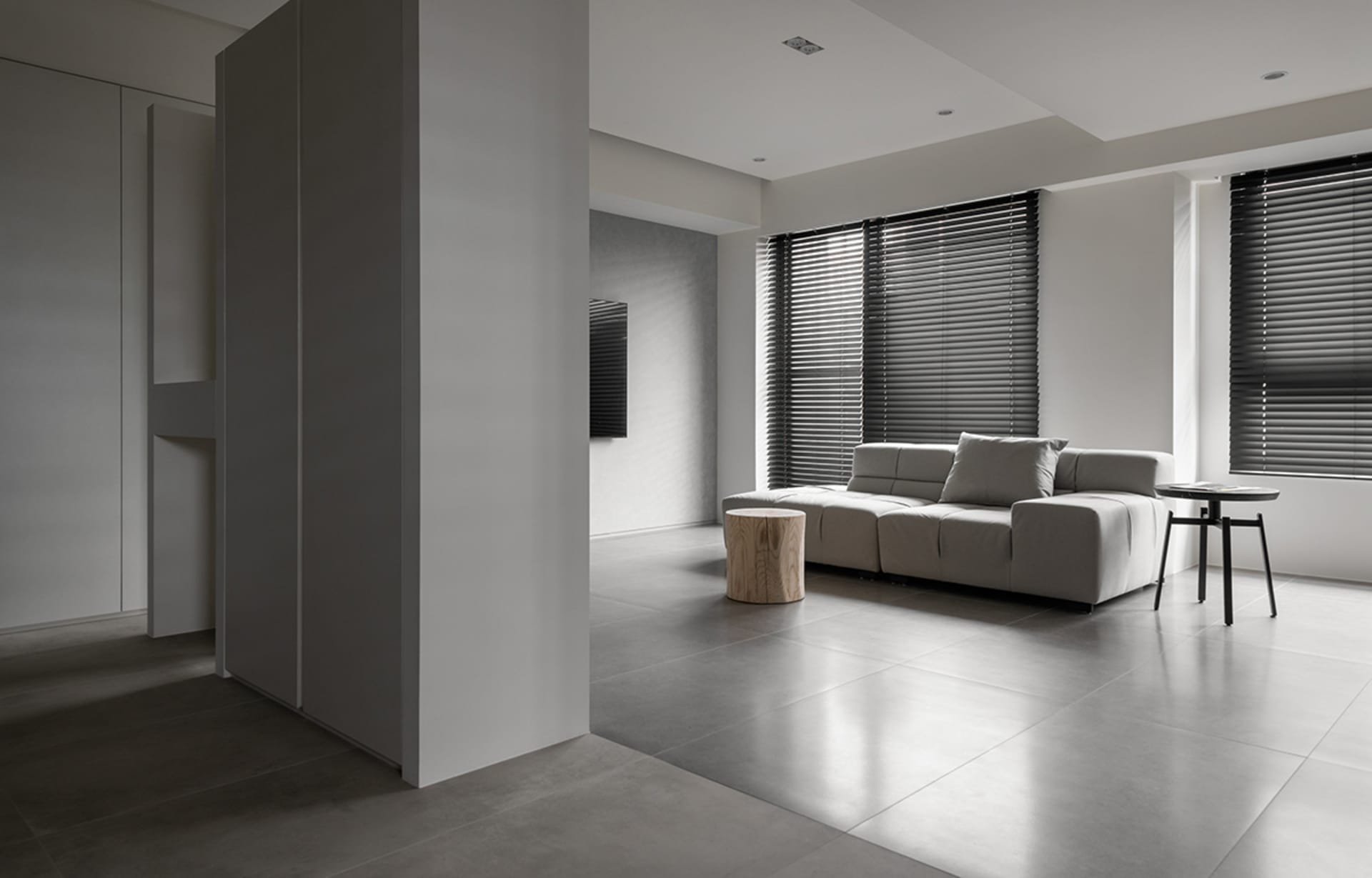 Modern minimalist living room with concrete flooring, a gray sofa, and black window blinds.
