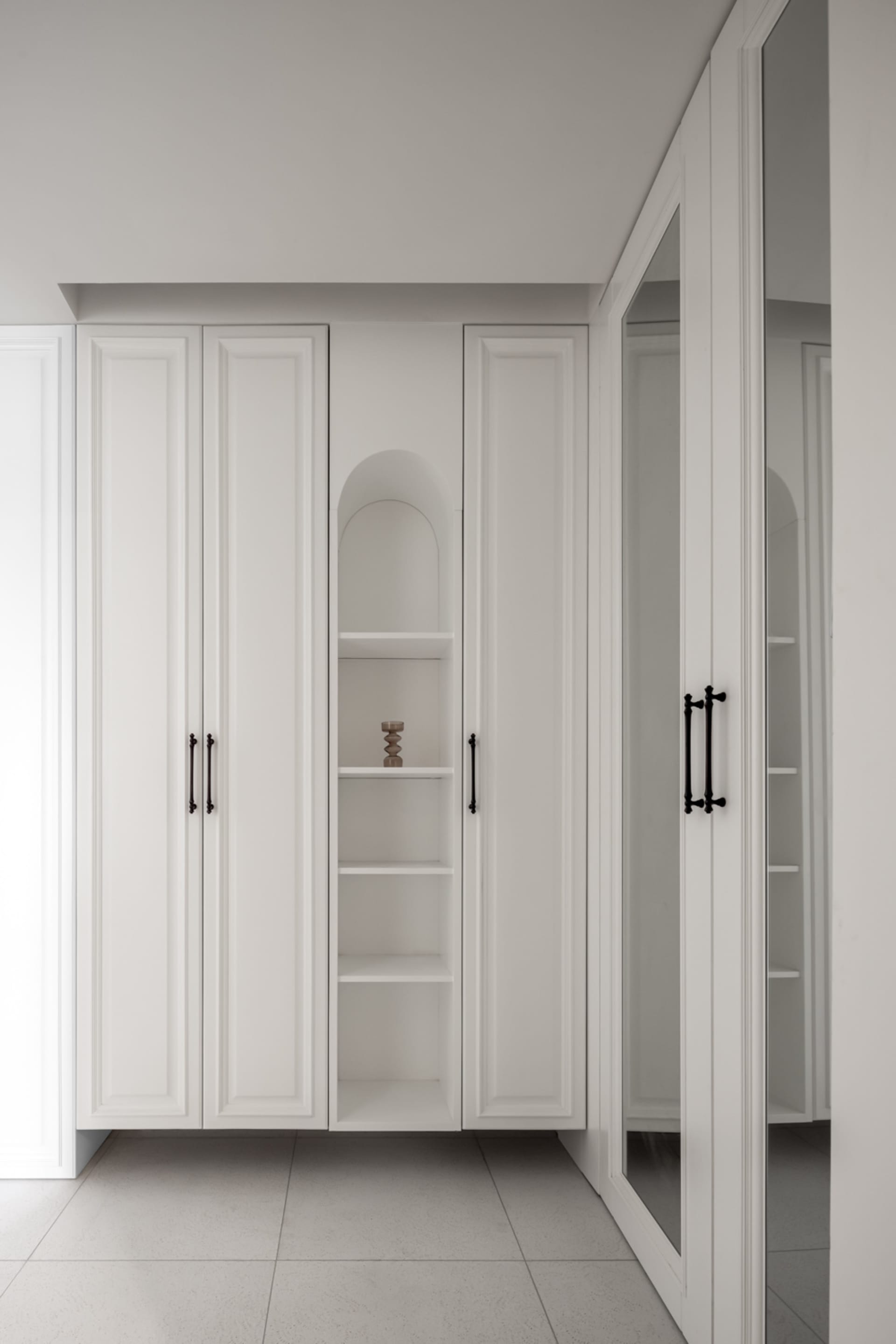 A minimalist white closet with sleek black handles and a small decorative object on the shelf