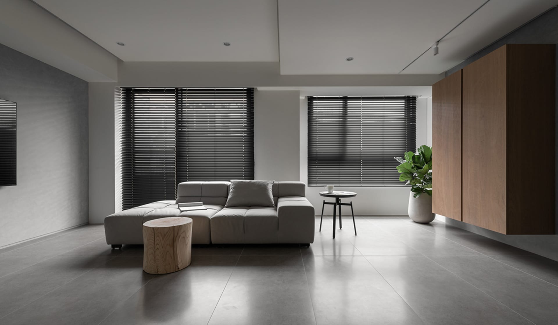 An elegant modern living room with gray minimalist furniture and concrete flooring, featuring large windows with dark blinds.