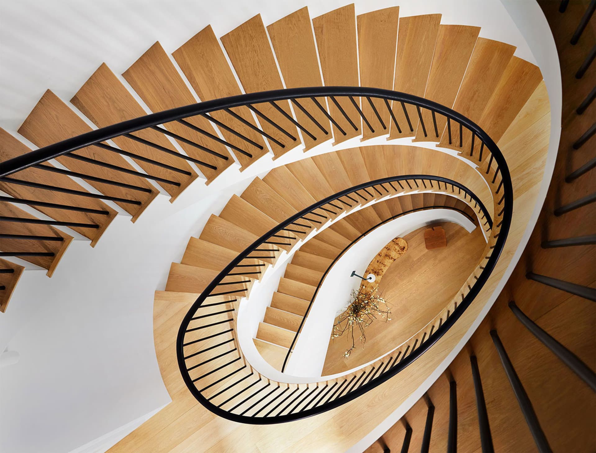 A modern, wooden spiral staircase with black railings and white walls.