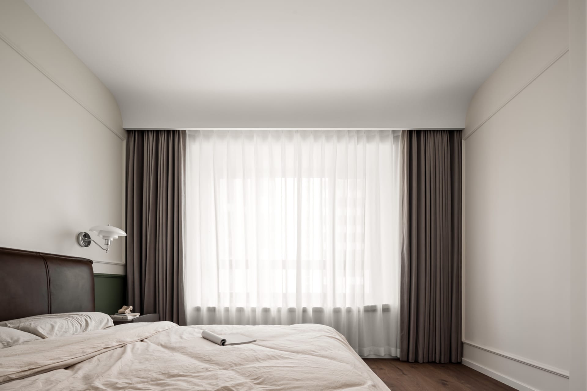 A minimalist bedroom featuring fabric curtains and wooden floors.