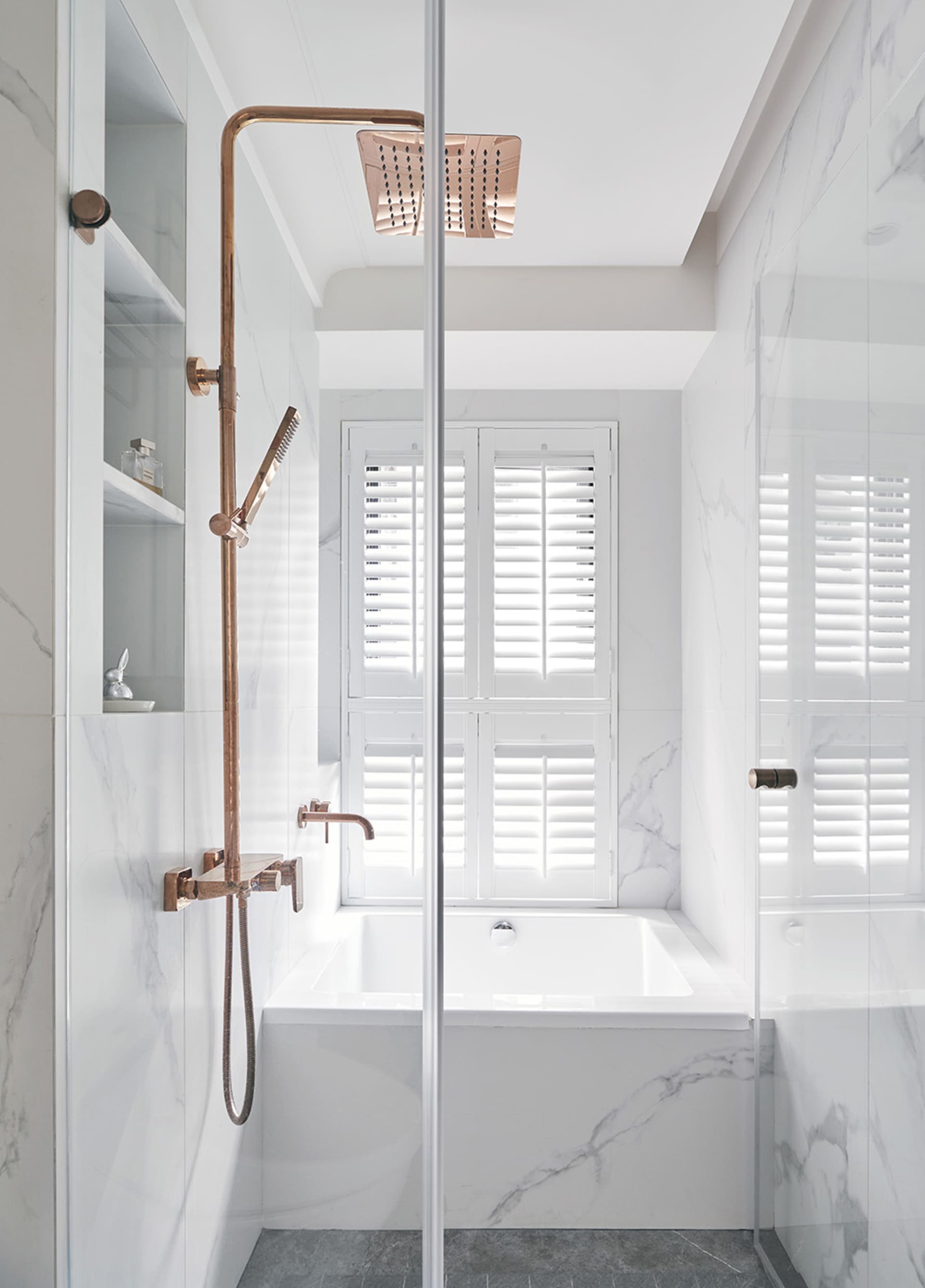 A modern minimalist bathroom featuring marble fixtures and a white bathtub with a window view.