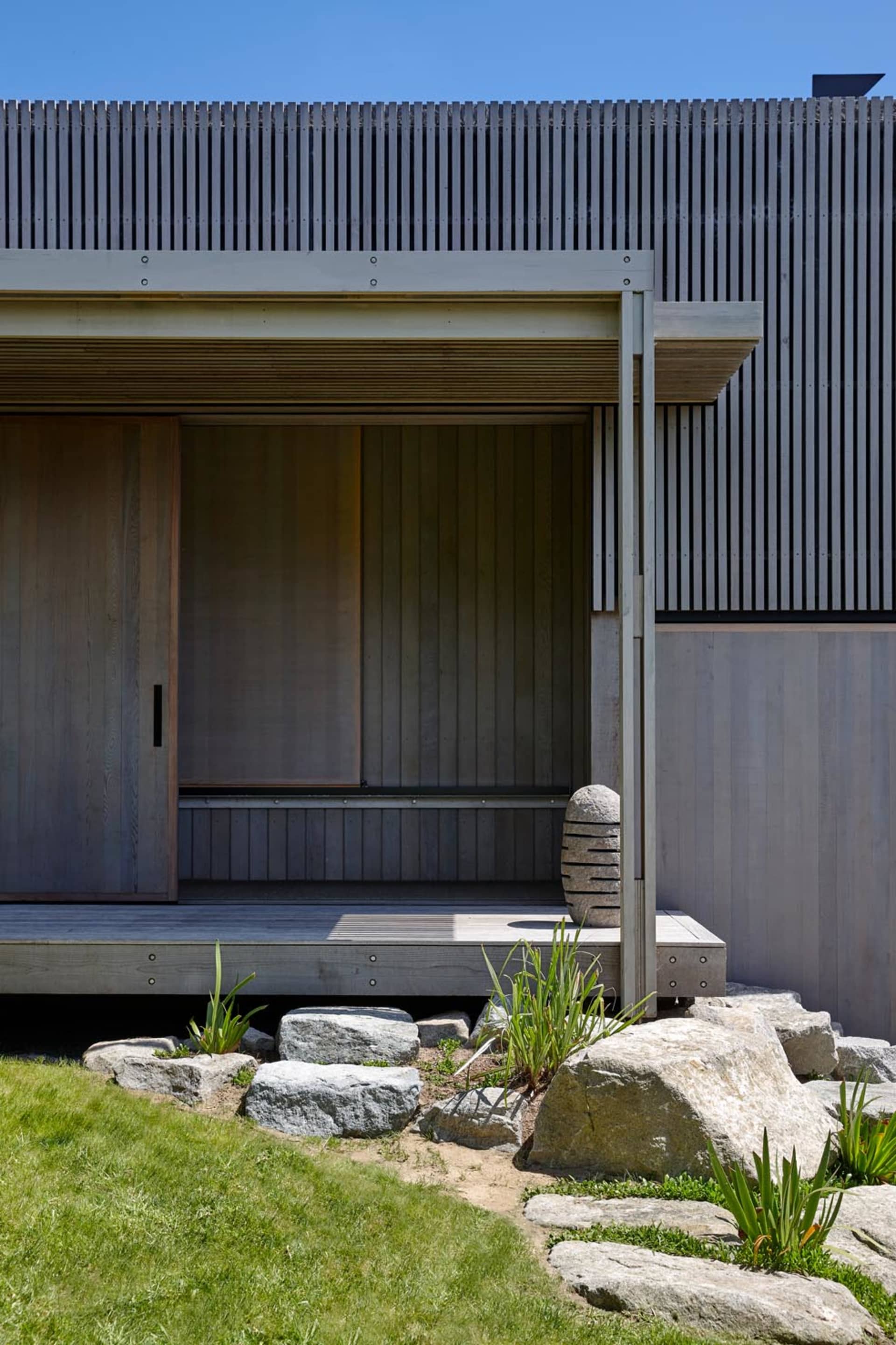 Modern exterior of a wooden house with a stone pathway and green grass.