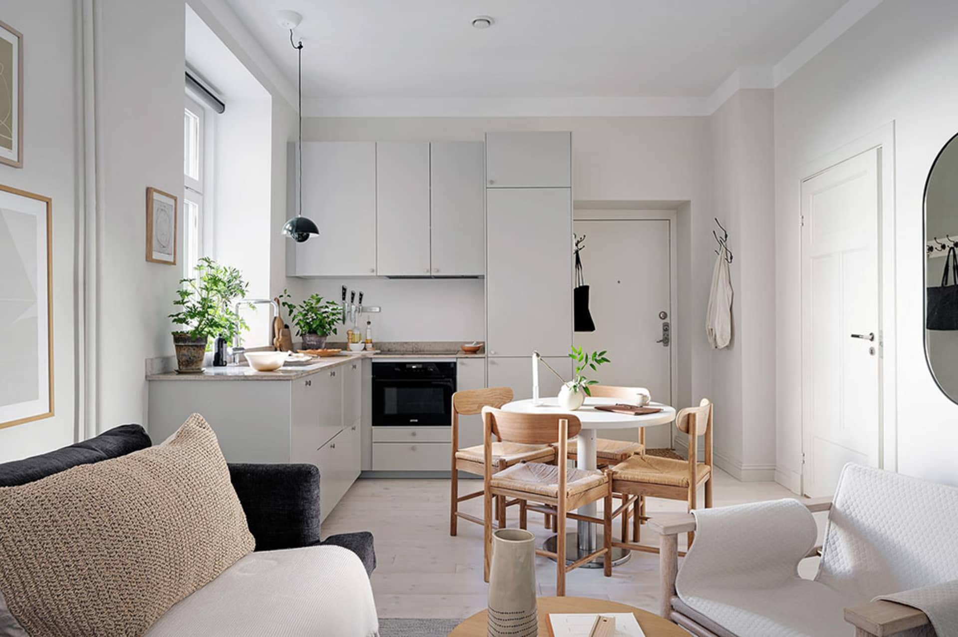 Modern, minimalist kitchen with neutral-colored cabinets, black appliances, and light wooden furniture.