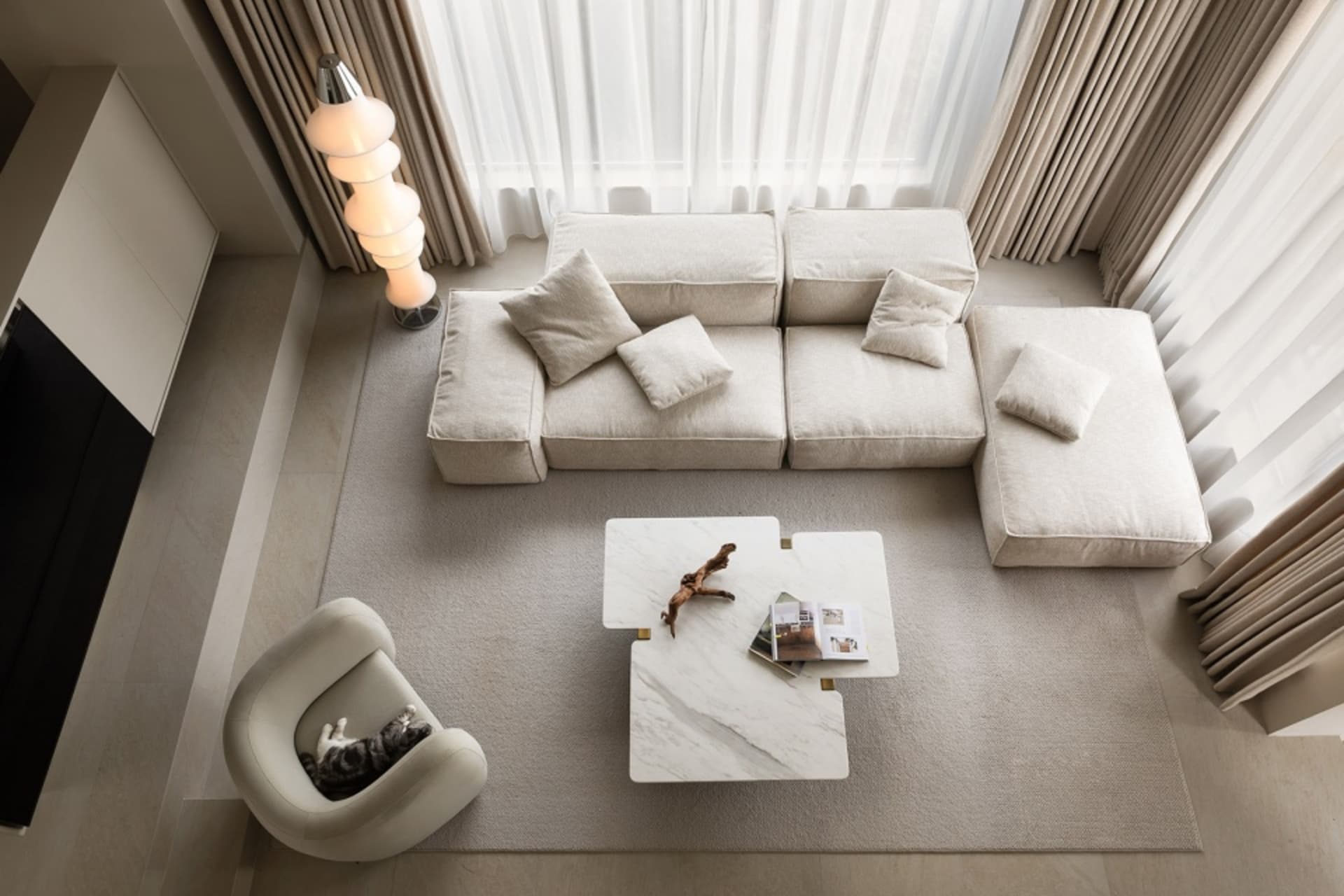 A stylish, minimalist living room with a white modular sofa, marble coffee table, and a cat lounging on a chair.