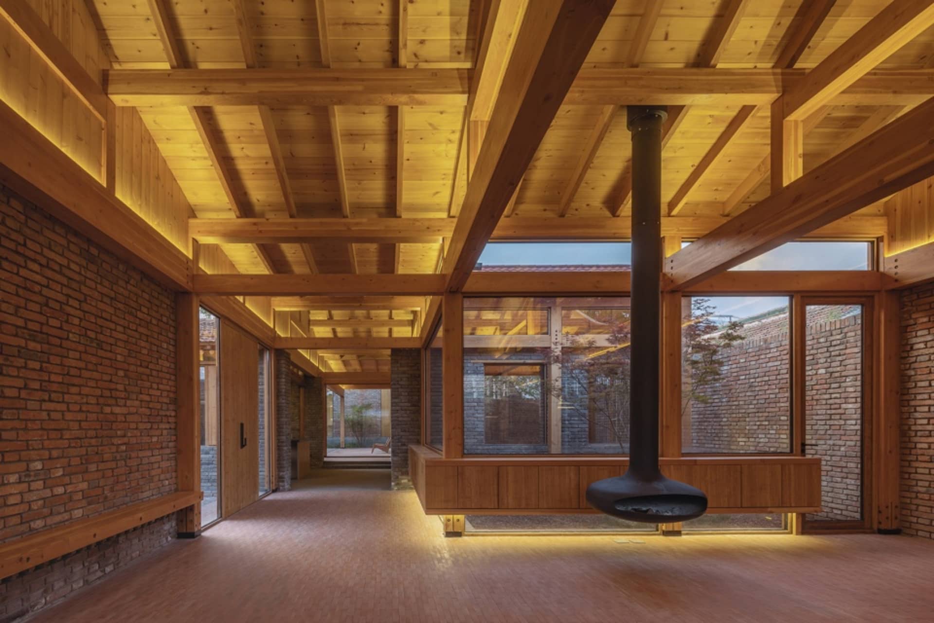 Modern living room with wooden ceiling beams, large windows, and a central fireplace.