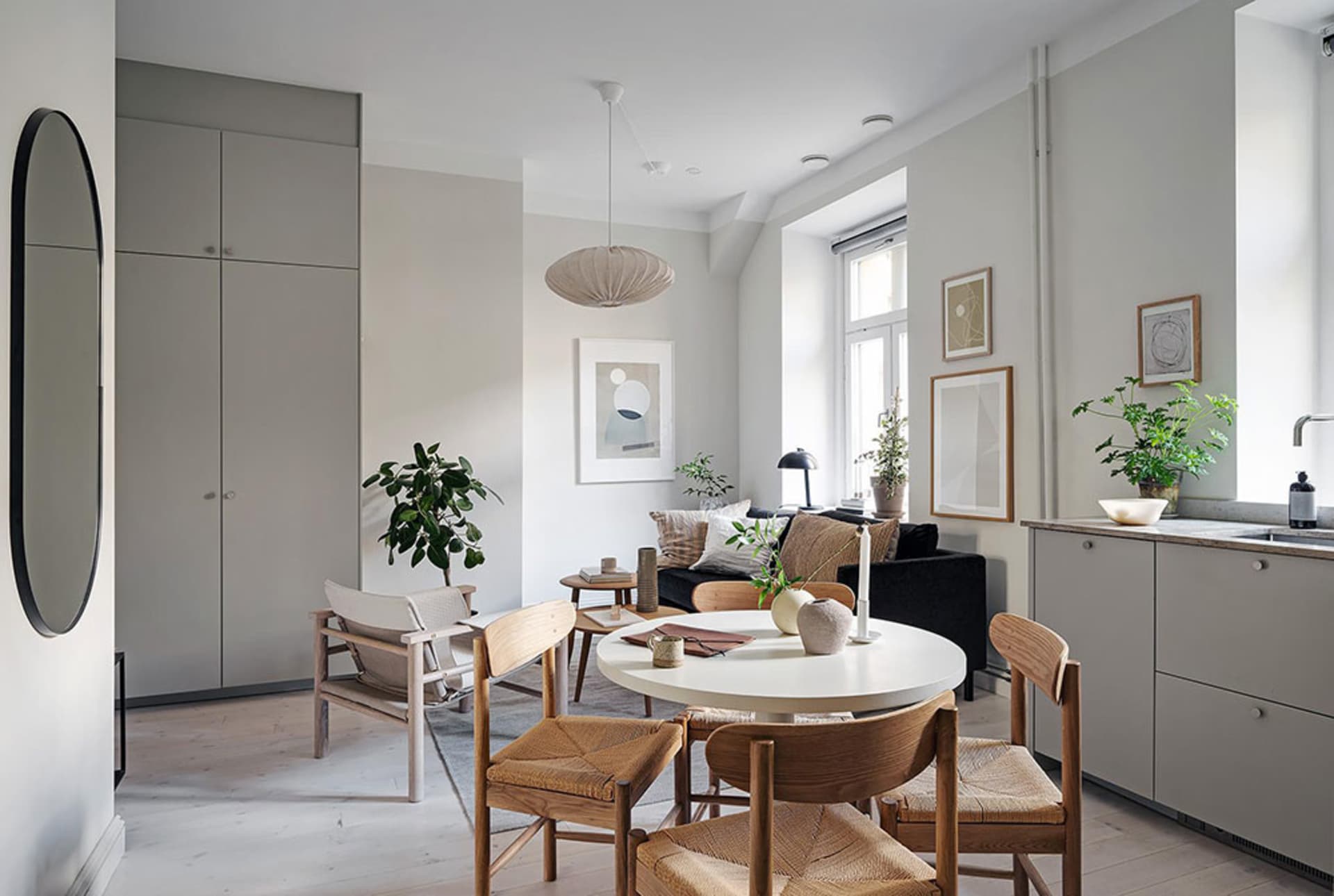 A well-lit, modern minimalist living room with white walls, light wooden flooring, and mixed materials like wood, glass, and