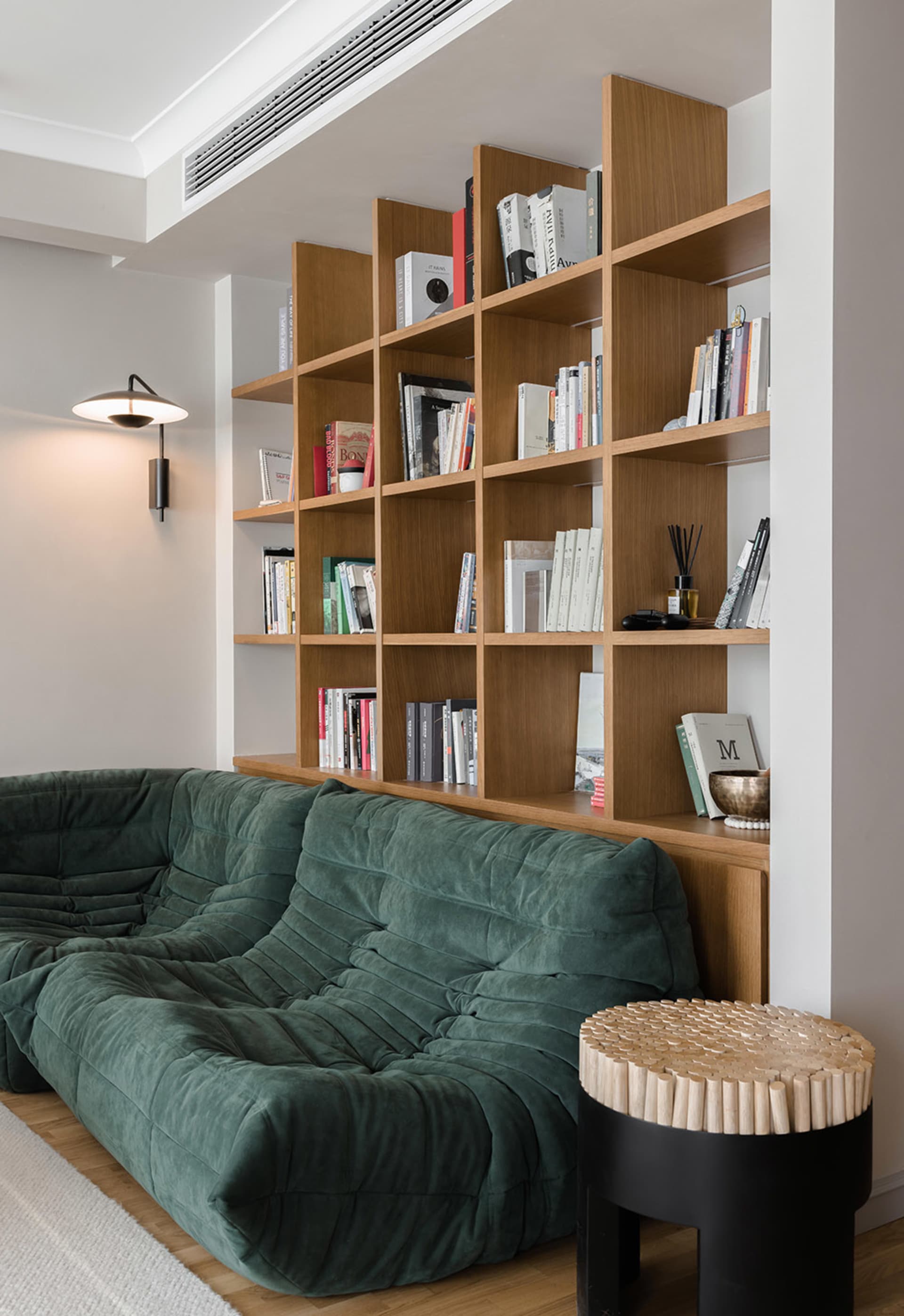 Modern industrial living room with a green plush sofa, wooden shelves filled with books, and a unique side table with a cylin