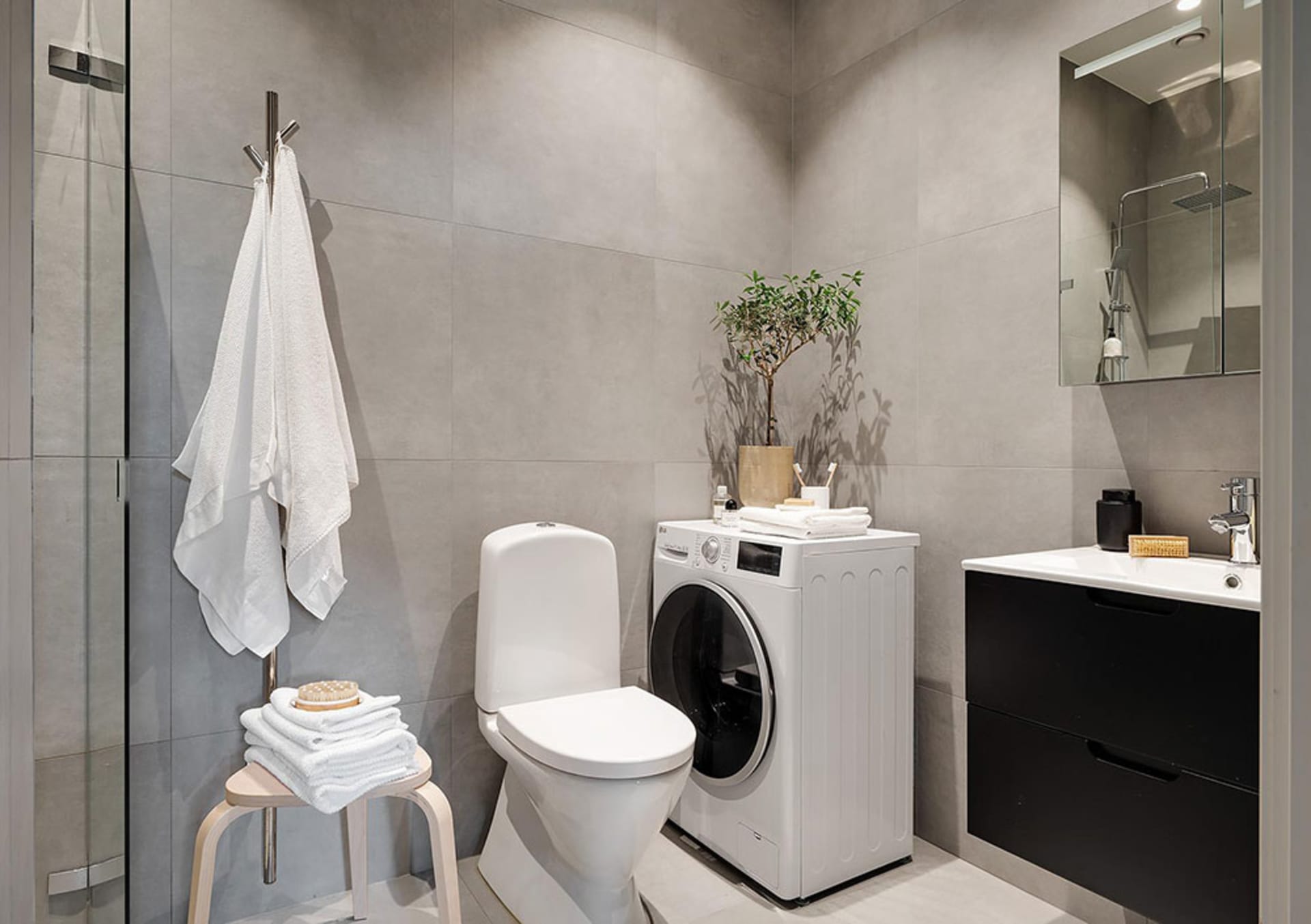 Modern minimalist bathroom with concrete walls, white toilet, white washing machine, black sink cabinet, and white towels.