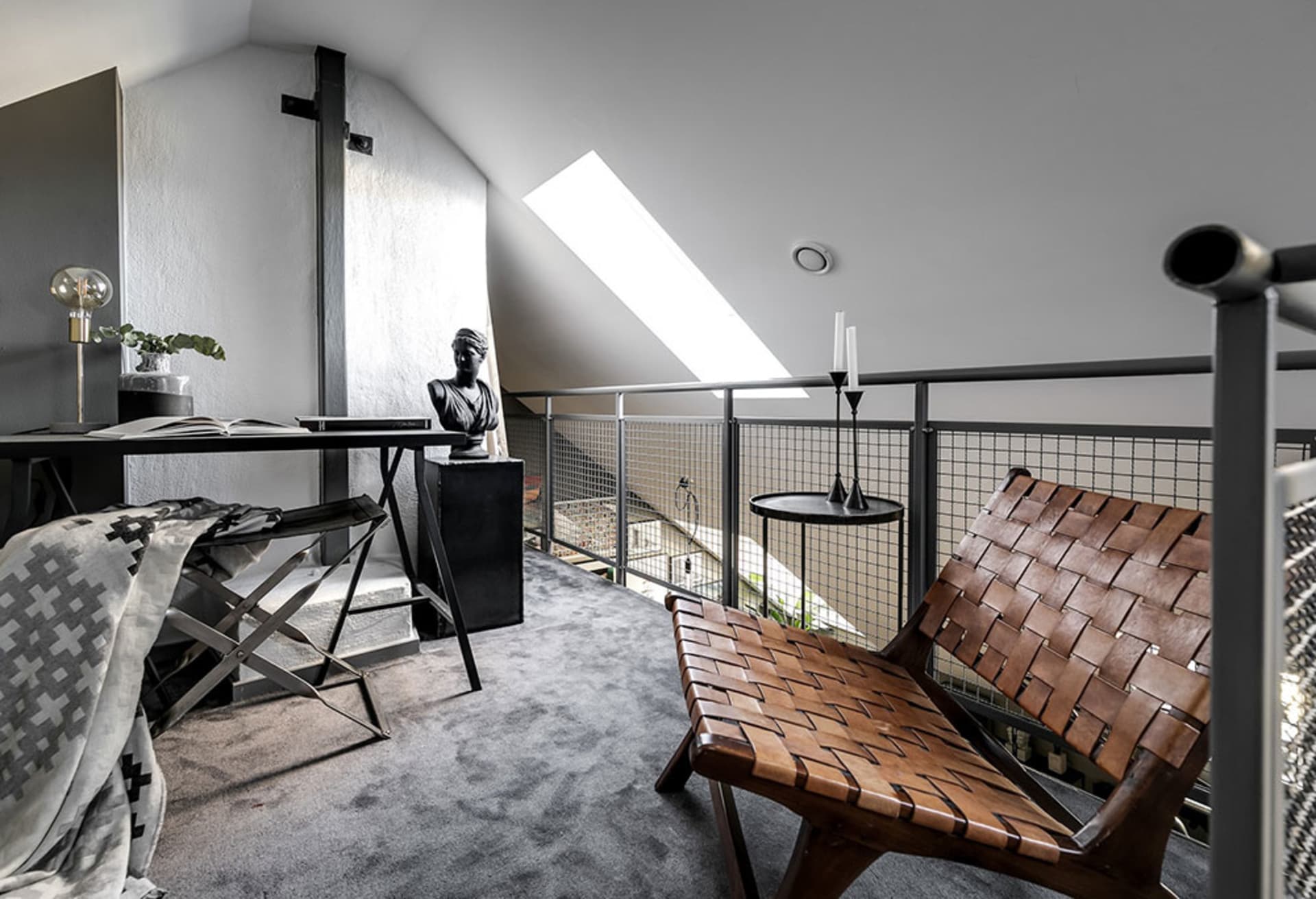 A modern home office featuring a metal desk, wooden chair, and glass balcony railing.
