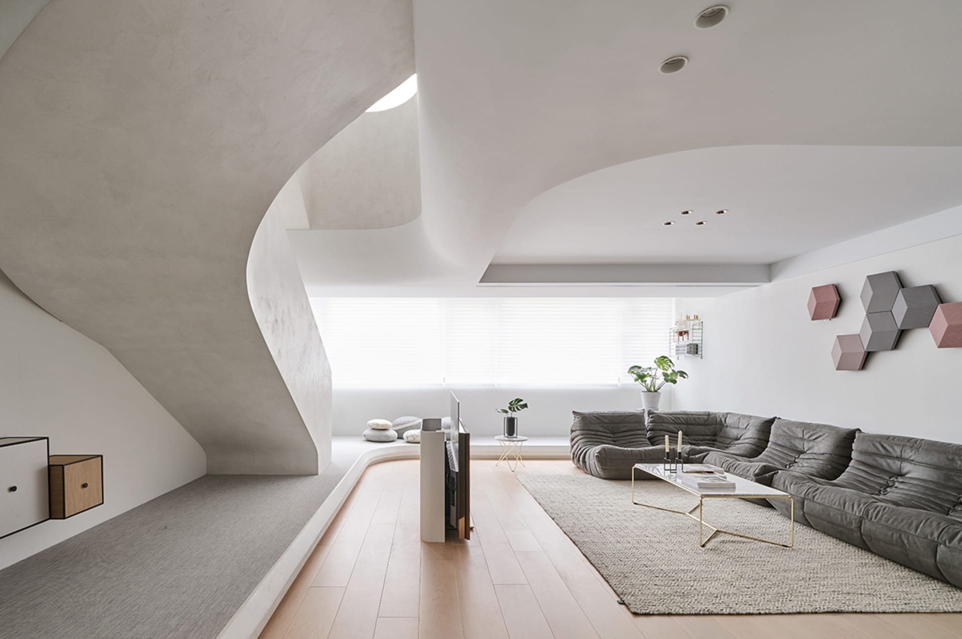 A modern living room with concrete walls, wooden flooring, and a gray textile sofa.
