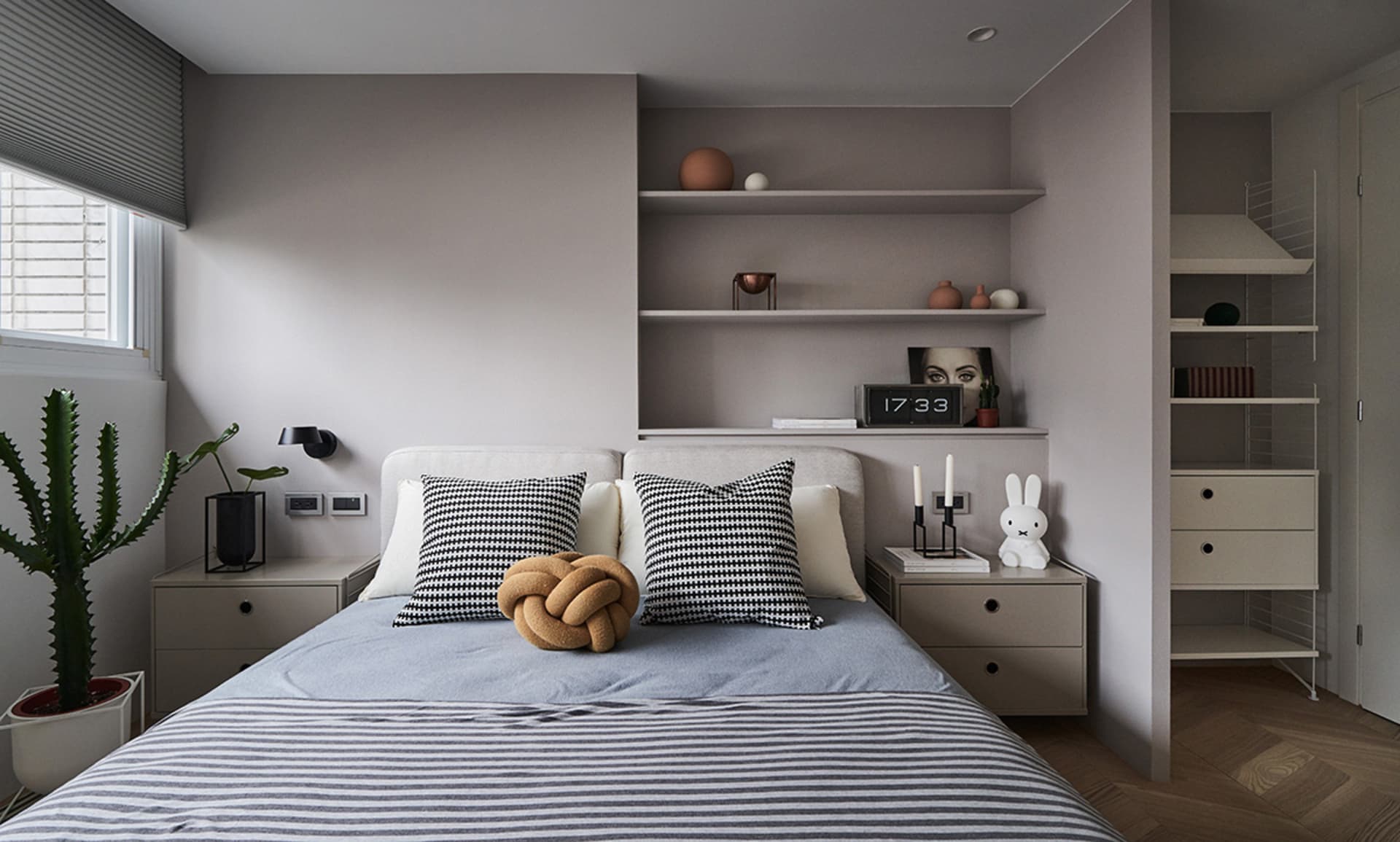 Minimalist bedroom featuring a bed with striped bedding, houndstooth pillows, and a knotted cushion, alongside a nightstand w