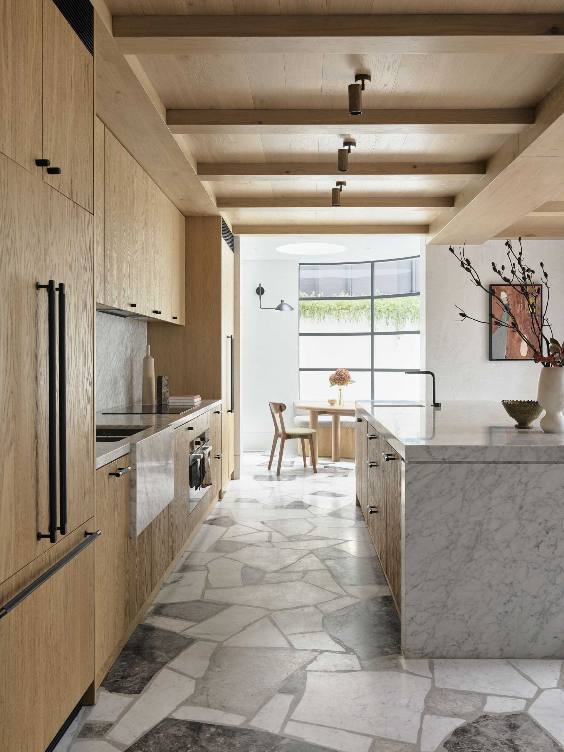 A modern minimalist kitchen with wooden cabinets, marble countertops, and natural light.