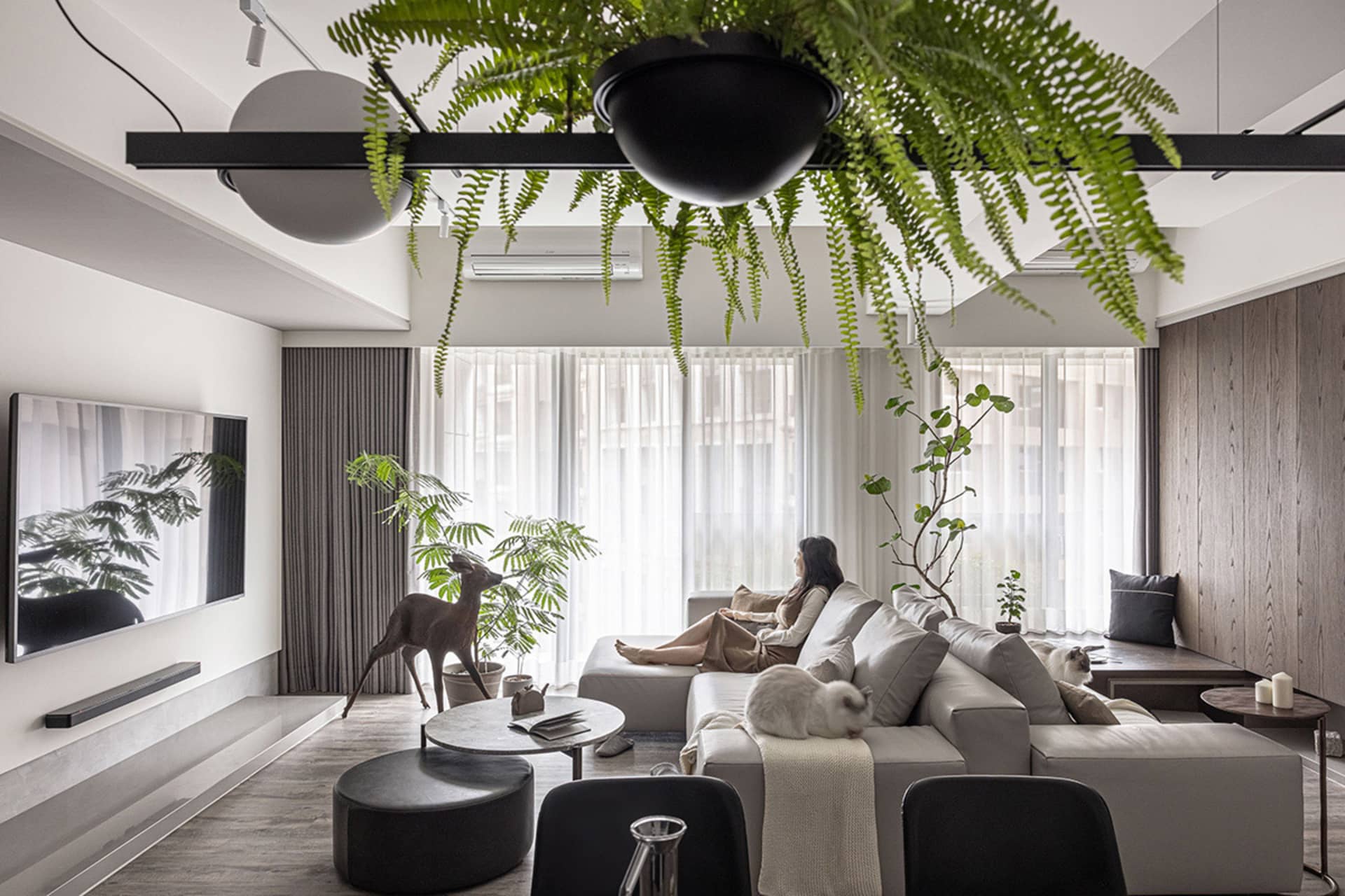 Modern, minimalist living room with concrete elements, plants, and a woman relaxing on a sofa.