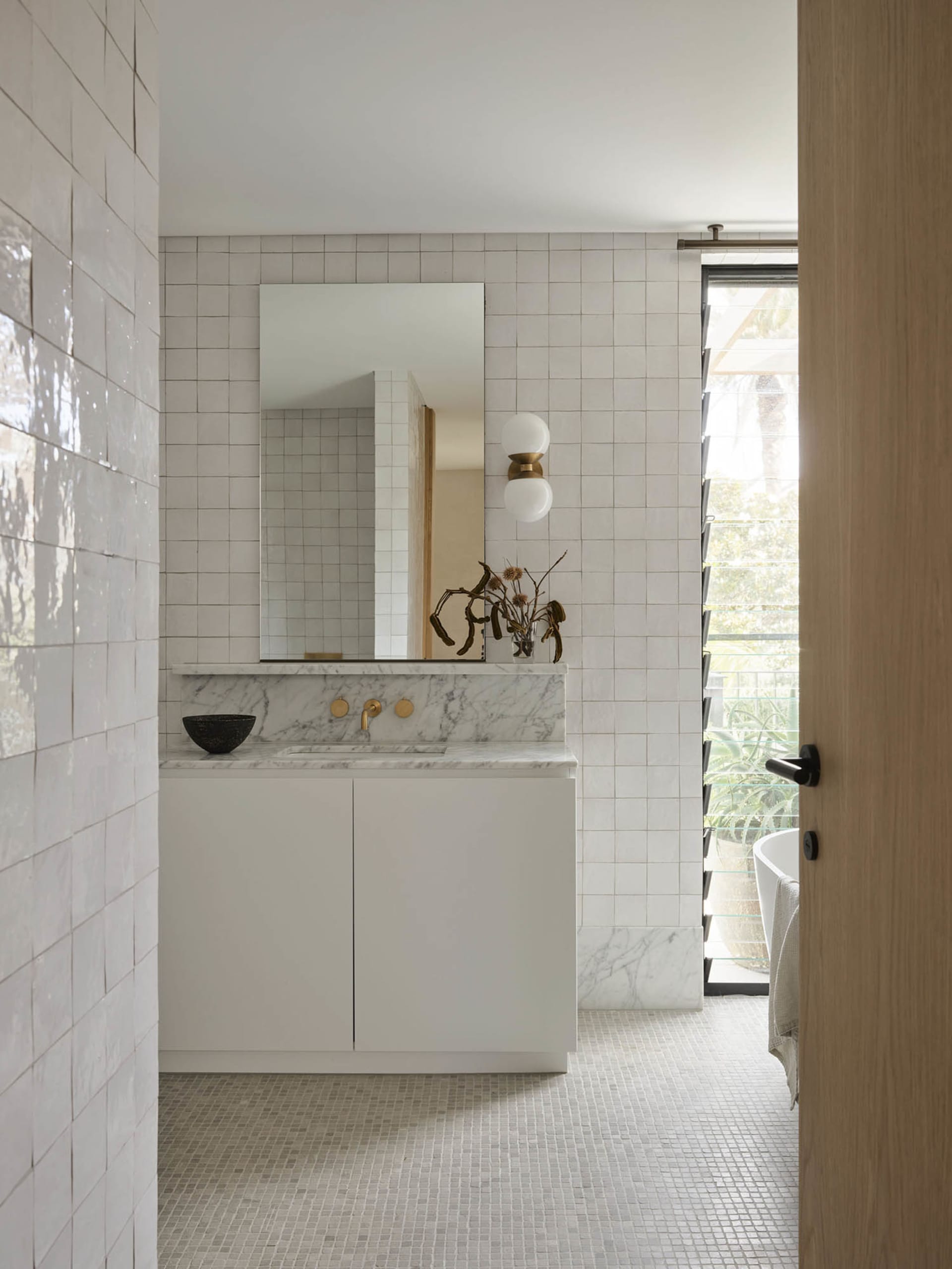 Modern bathroom with marble tiles, white cabinetry, and a sink with brass fixtures.