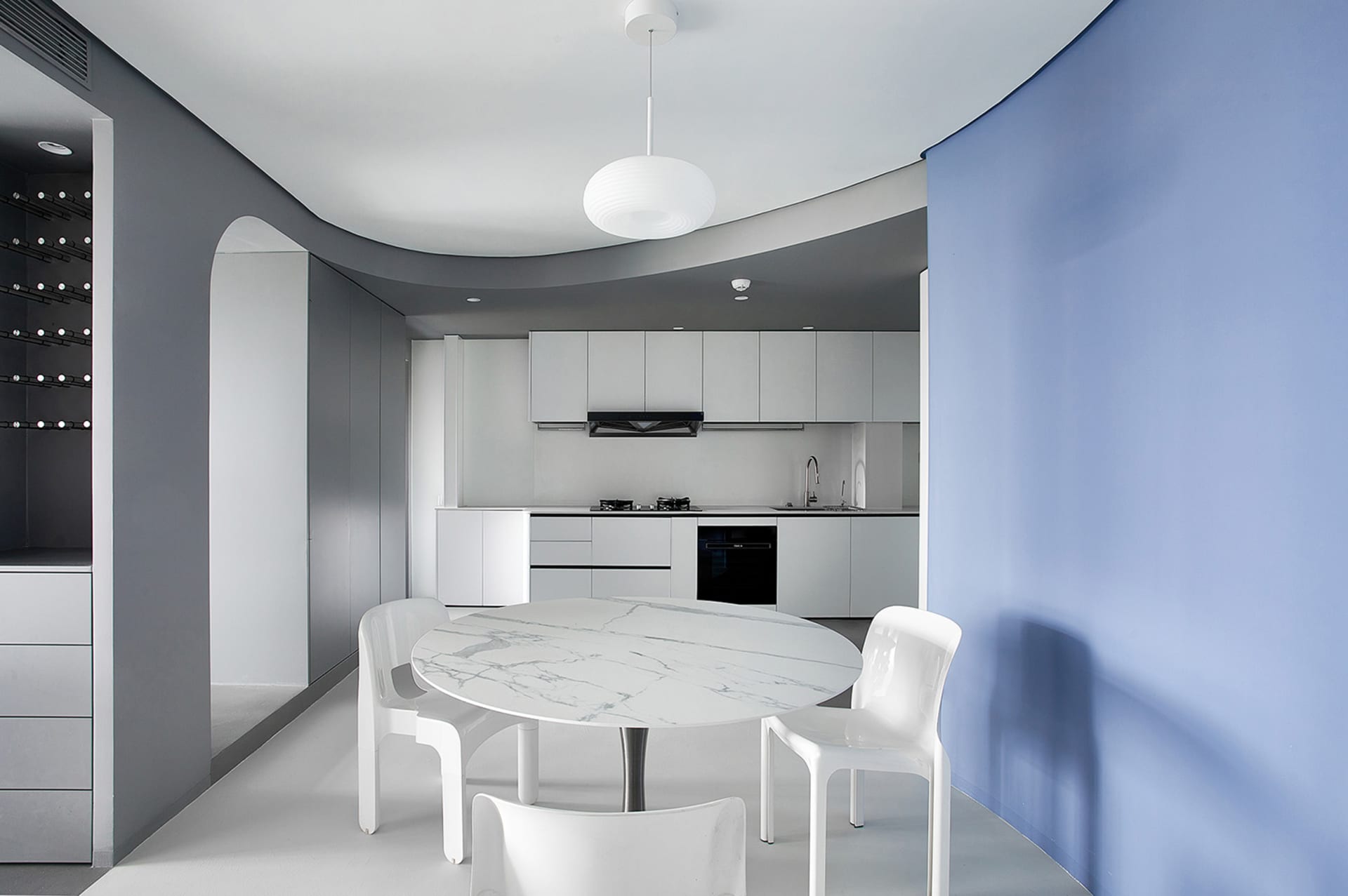 A modern kitchen and dining room with white marble table and chairs, white walls, and white cabinets.
