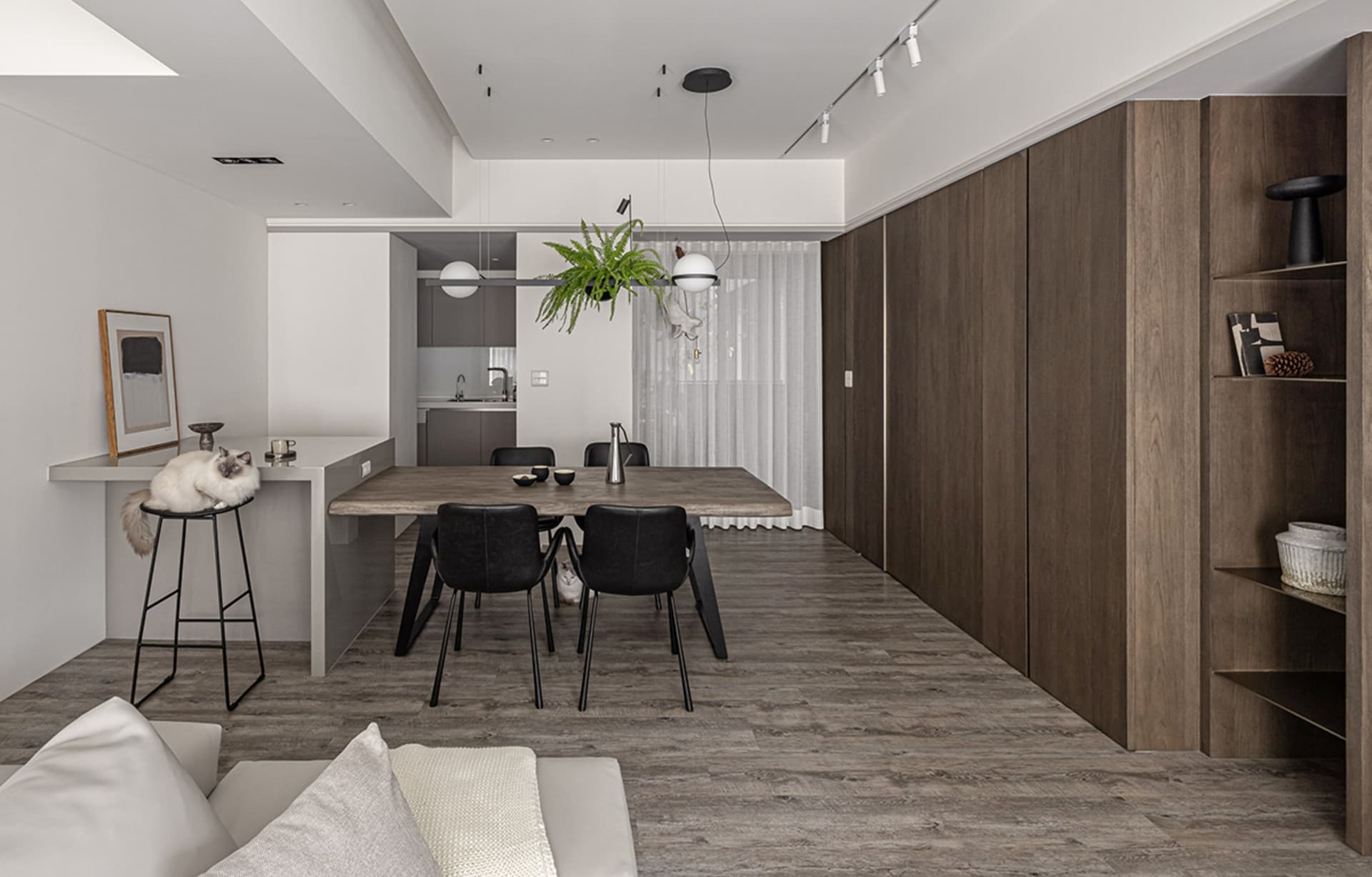 A modern living and dining room featuring a wooden table, black chairs, and a wooden shelving unit.
