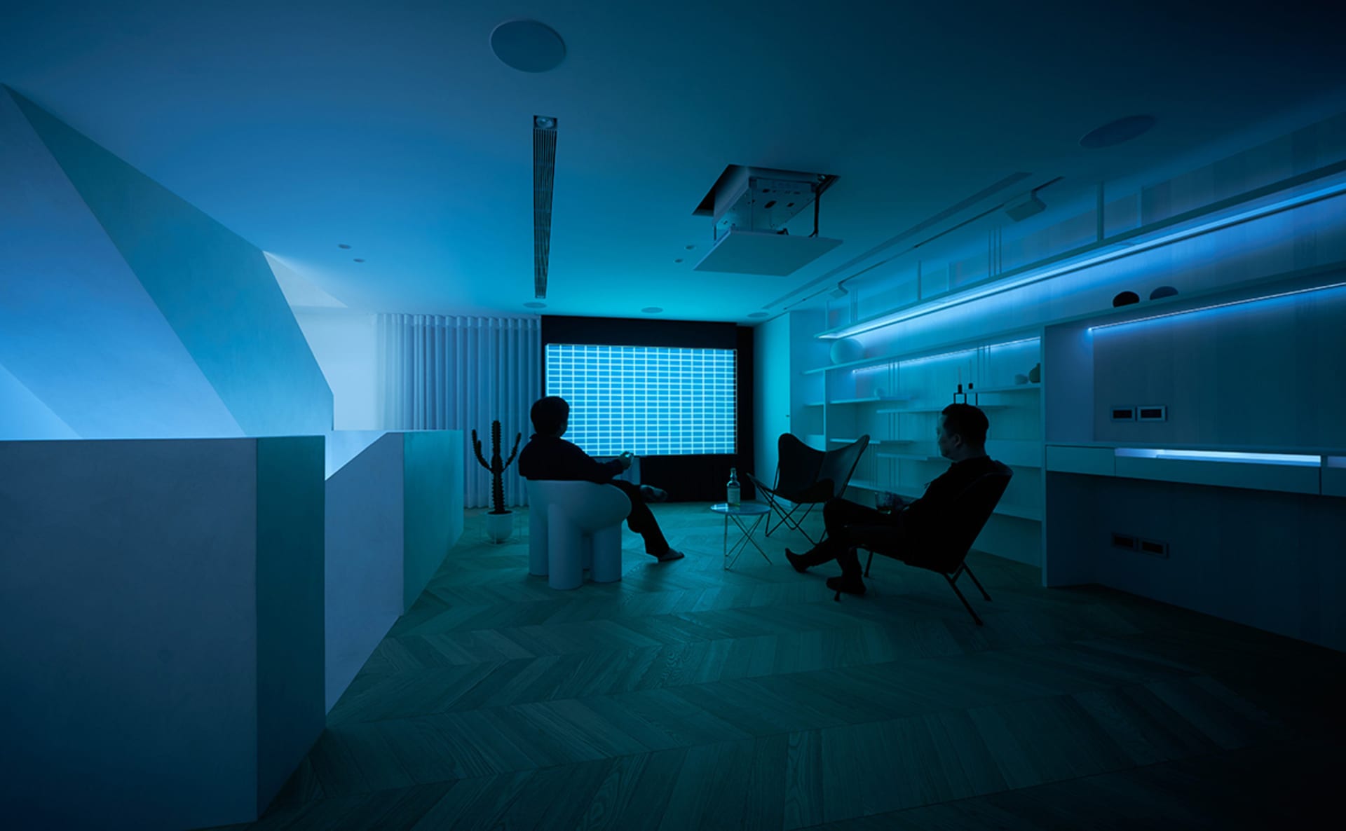 Two individuals sitting in a modern living room with metallic elements and a blue light setting.