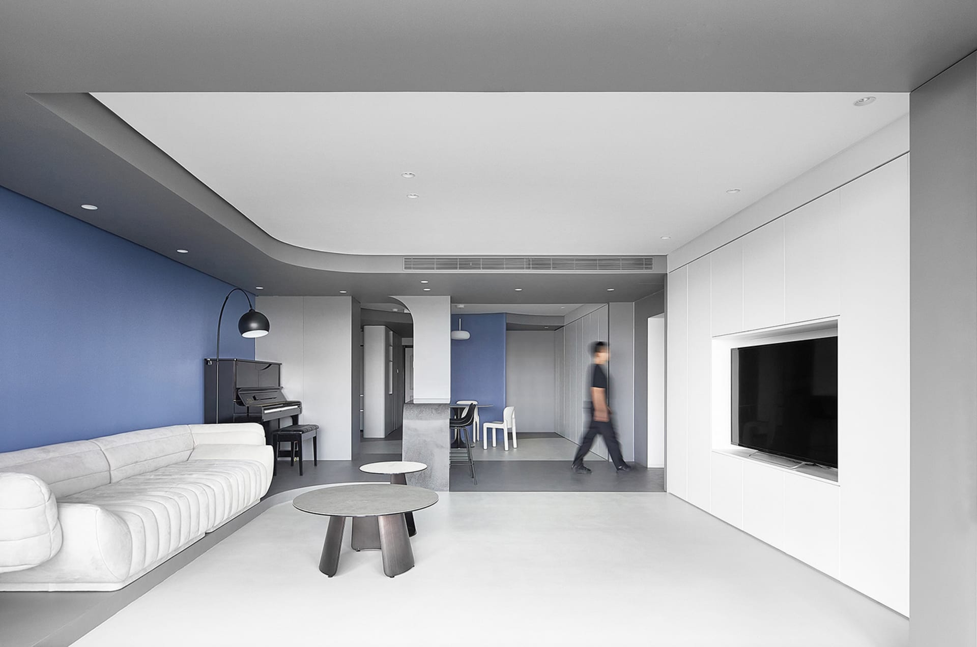 A modern, minimalist living room featuring a white sectional sofa, concrete flooring, and a piano in the corner.