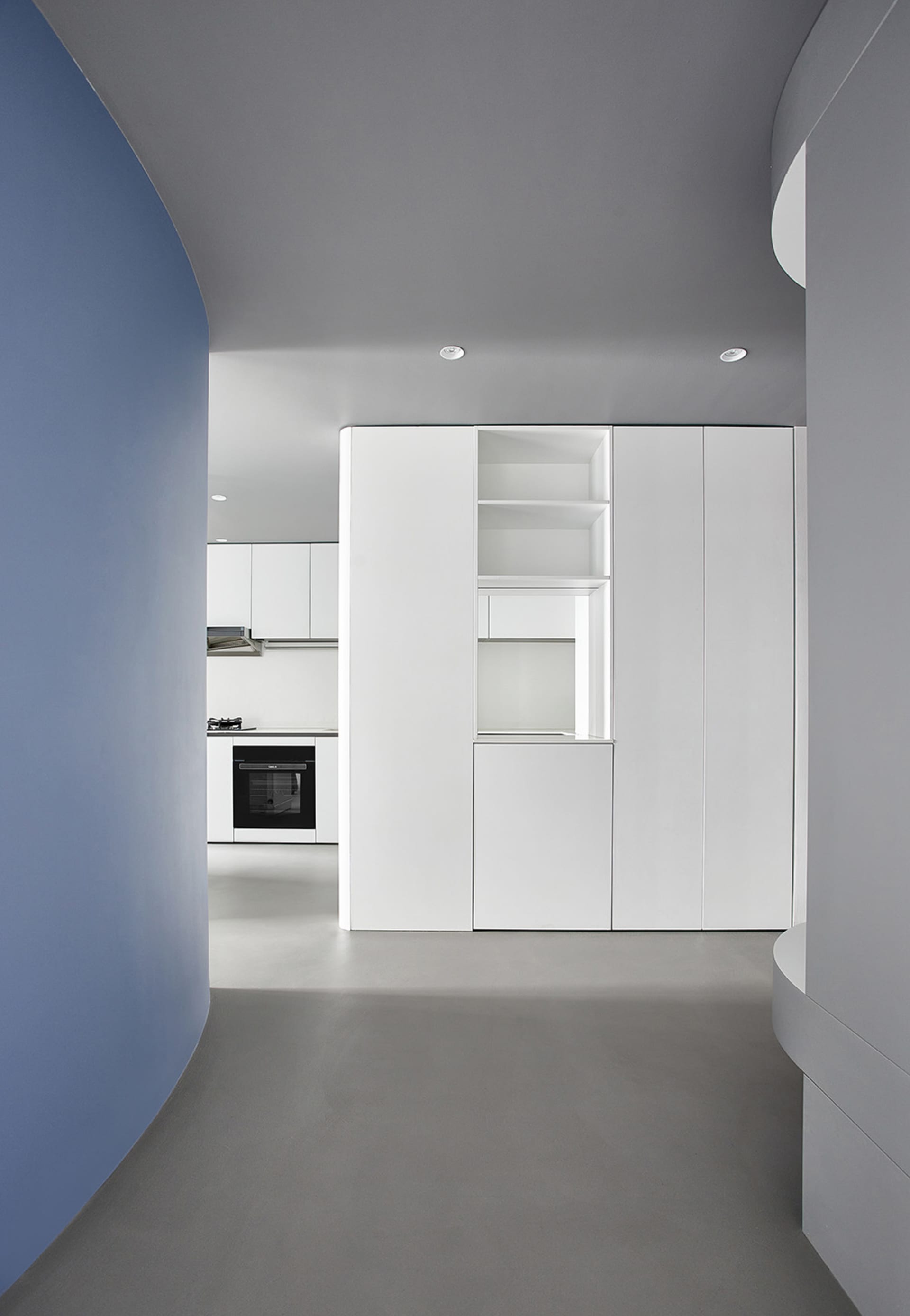A modern, minimalist kitchen with white cabinets, concrete floor, and white walls.