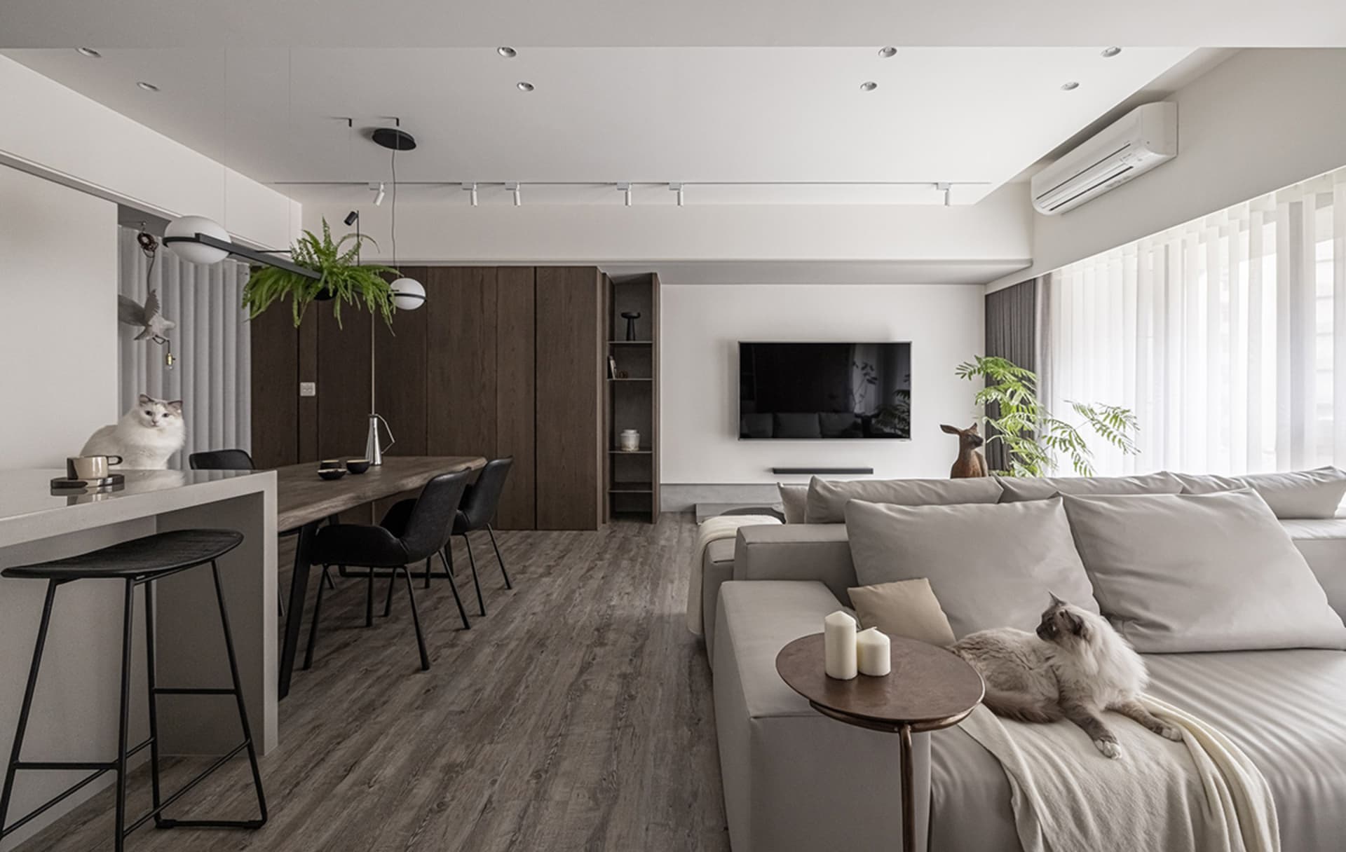 A minimalist living room with neutral-toned furniture and decor, featuring a comfortable sofa, a sleek dining area, and a fla