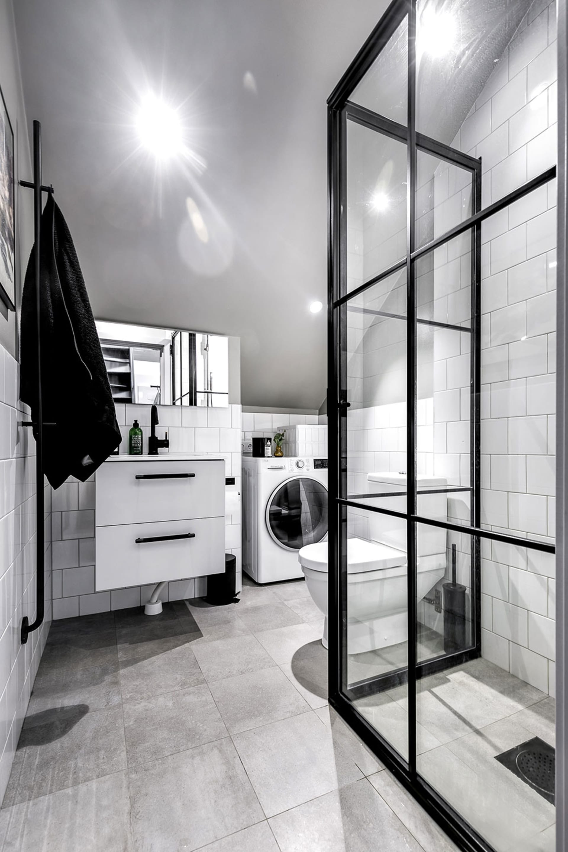 A modern monochrome bathroom with white tiles, black accents, and minimalist design.