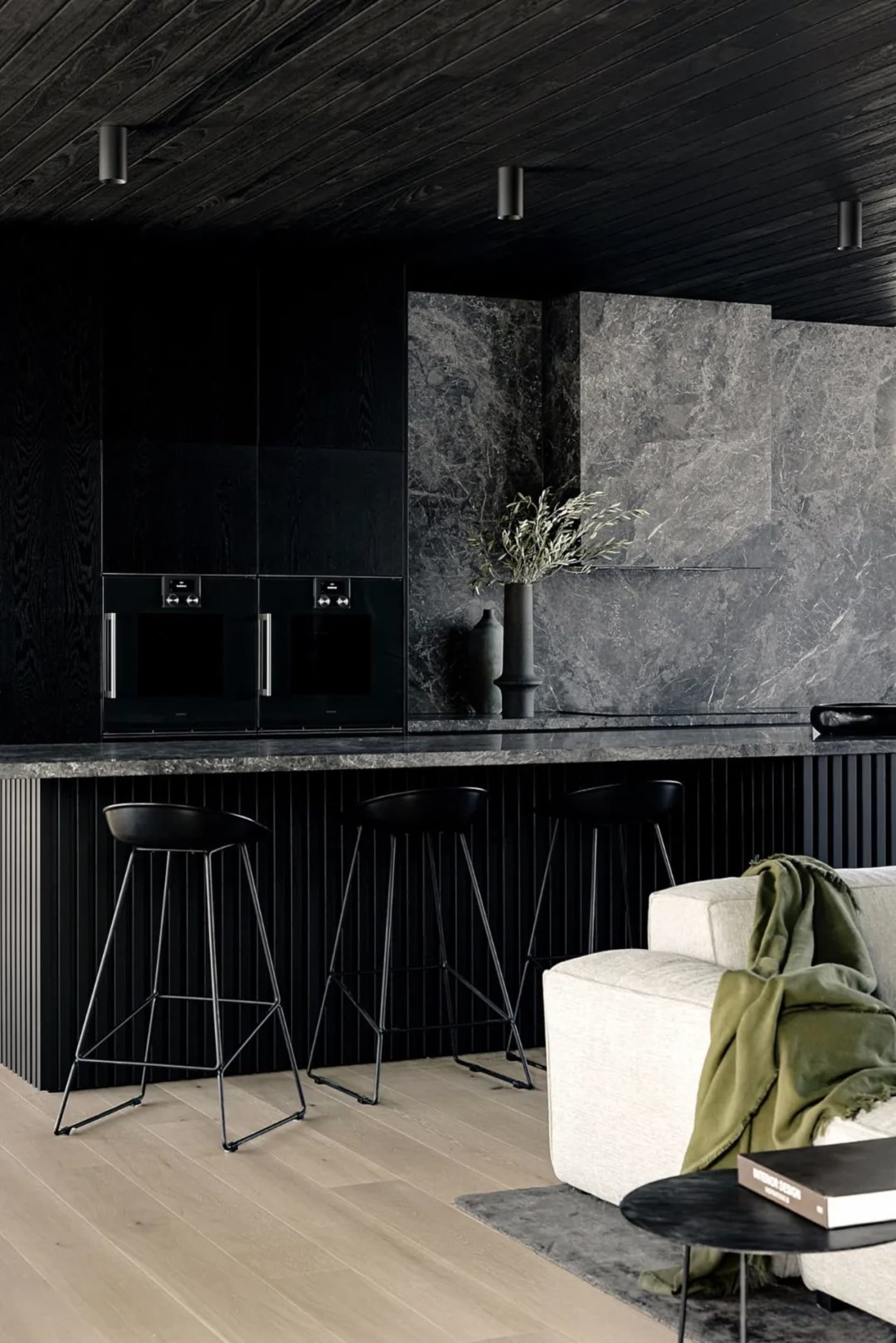 A minimalist residential kitchen showcasing a marble countertop and backsplash, with black stools and sleek black cabinetry.