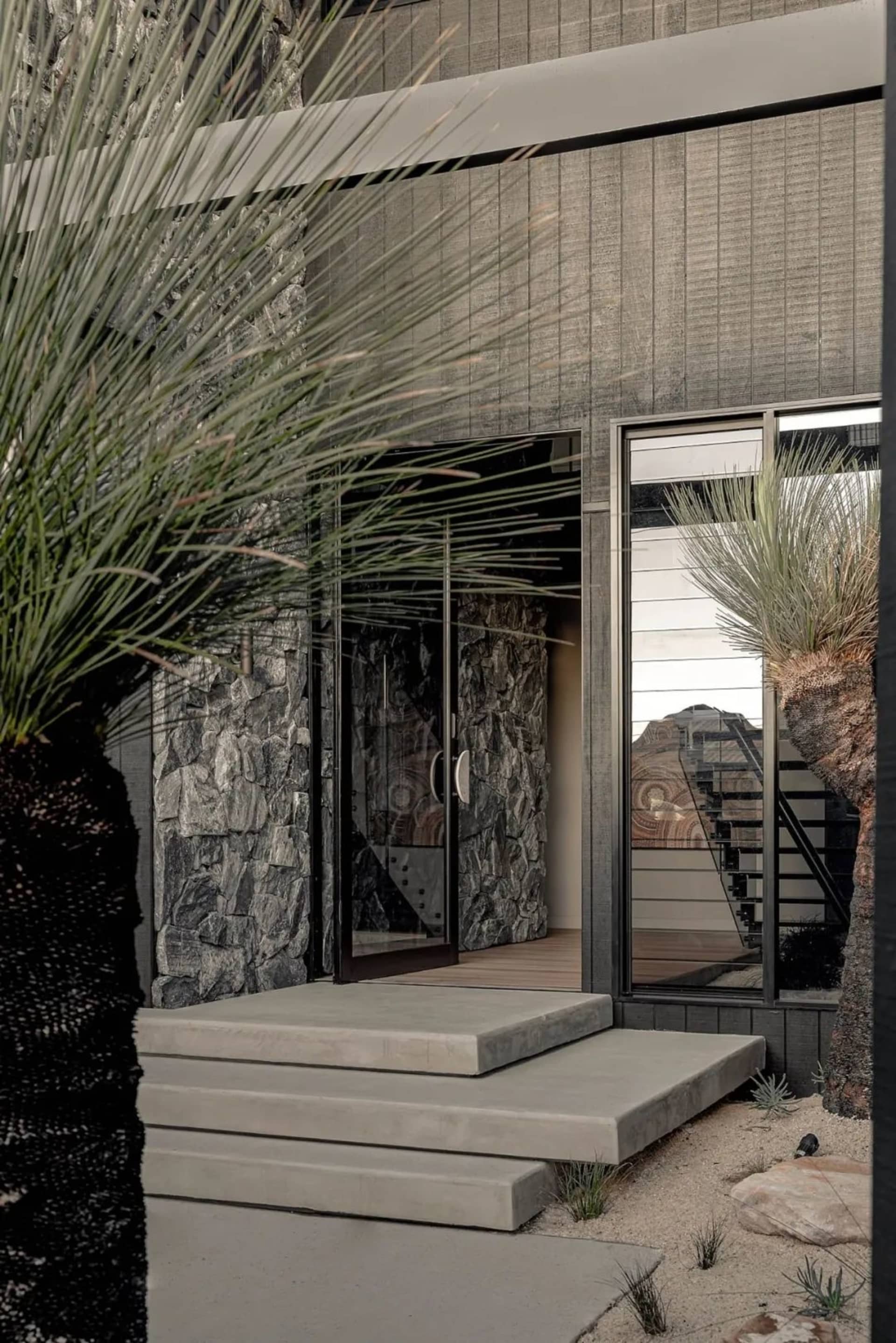 Concrete steps leading to a modern entrance with stone walls and glass door.
