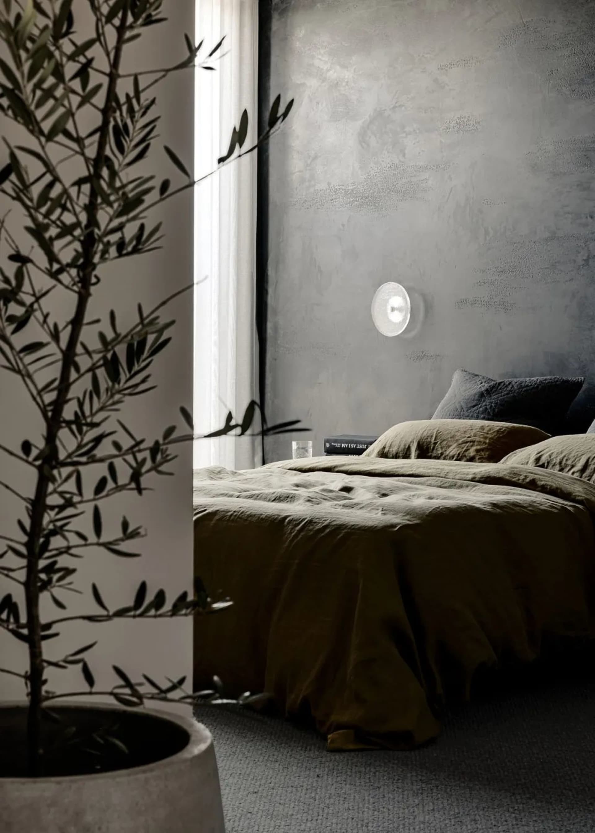 A minimalist bedroom featuring a concrete wall and bed with olive green bedding.