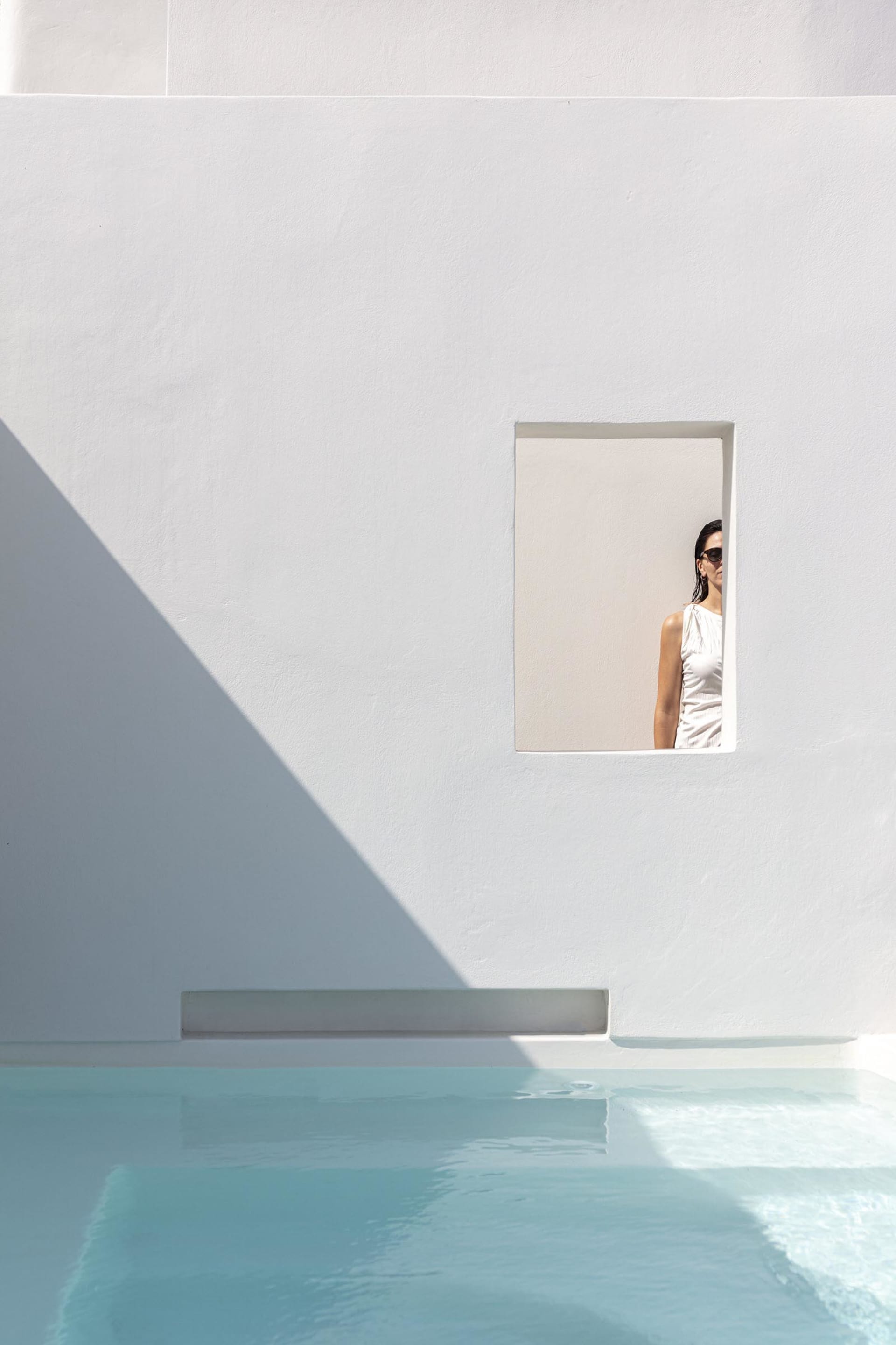 A minimalist design featuring a concrete pool side with a woman looking through a window.